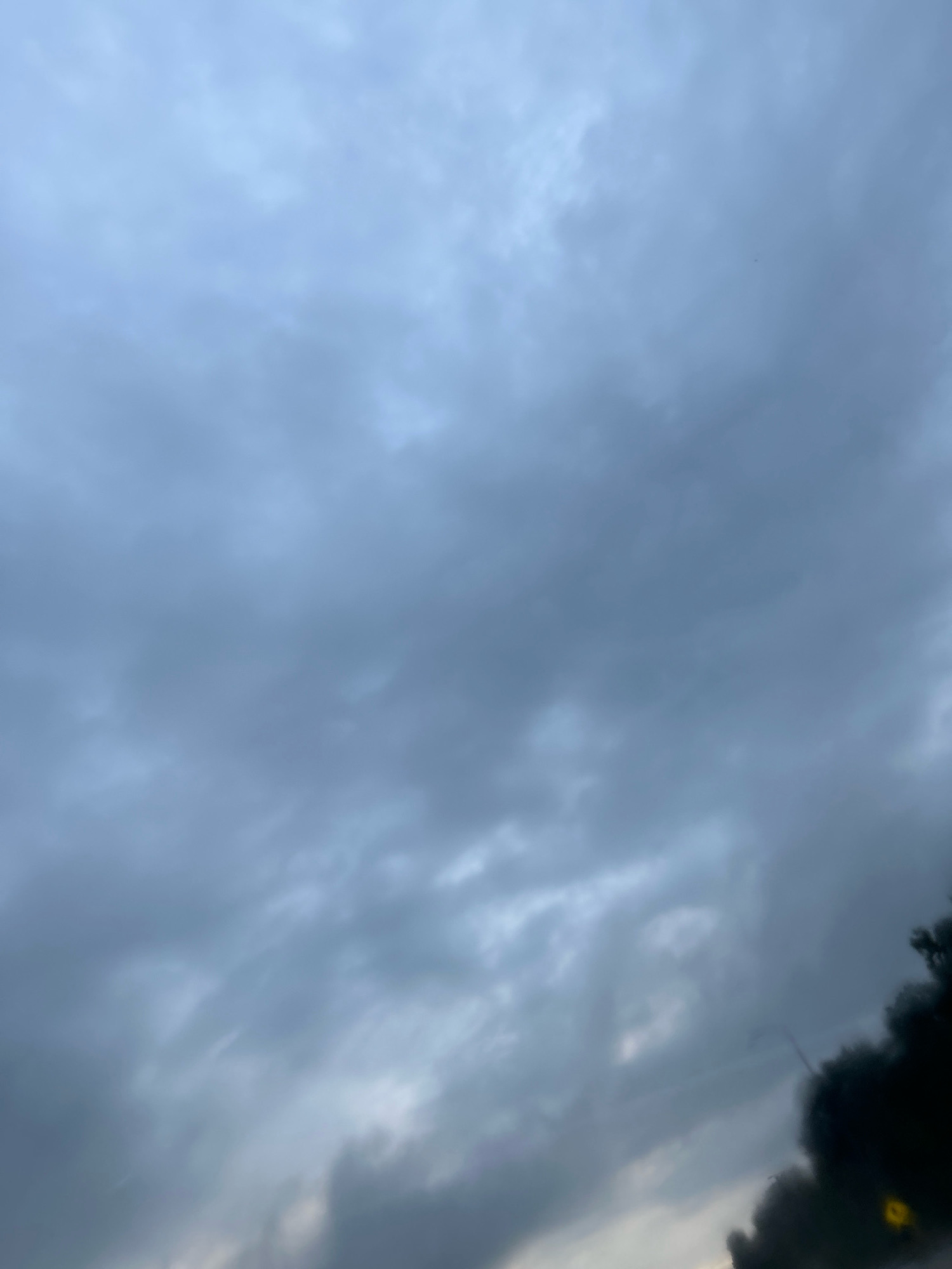 The image shows a cloudy sky in Robinson Township, United States of America. The clouds are dark gray and appear to be heavy with rain. The sky is overcast, and there is no sunlight visible. The bottom right of the image shows some trees and what appears to be a street light. The overall scene is dark and gloomy, suggesting a potential for rain or stormy weather.