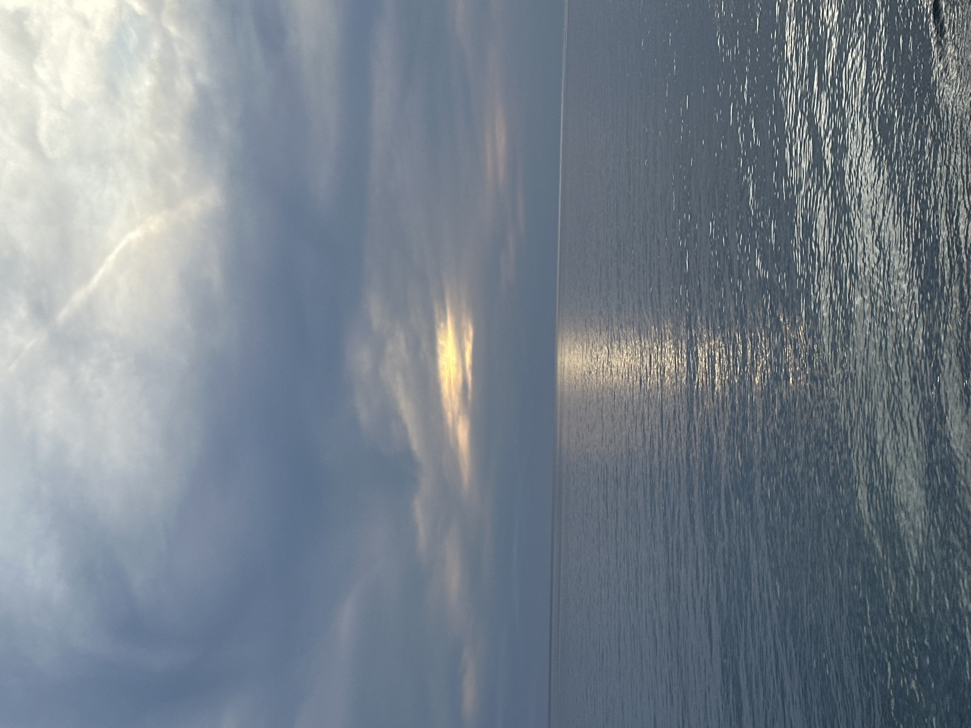 The image shows a seascape. The right side of the frame depicts the surface of the sea, reflecting sunlight. The left side shows a sky with clouds, also reflecting sunlight. The horizon line appears straight, suggesting a relatively calm sea state. No people, buildings, or other objects are visible. Given the prompt's context, the location is likely the sea in Bar, Montenegro.