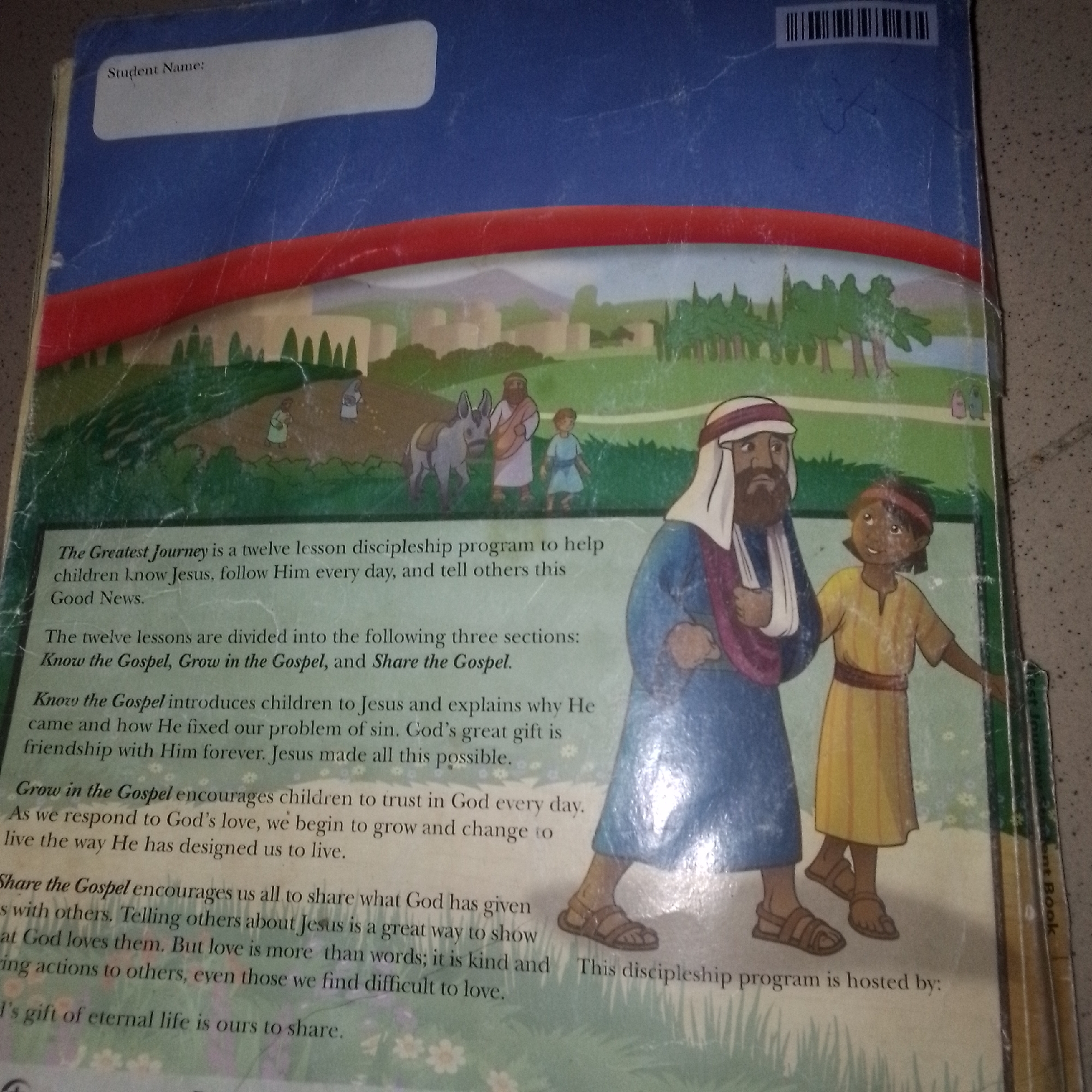 This image shows the back cover of a book titled "The Greatest Journey." The cover features an illustration of a biblical scene with several figures. In the foreground, two individuals, appearing to be a man and a child, are depicted walking. The man wears a white turban and a blue robe, while the child wears a yellow tunic. Behind them, a donkey and another figure are visible. The background illustrates a landscape with trees and buildings. Text on the cover describes the book as a twelve-lesson discipleship program for children, with sections titled "Know the Gospel," "Grow in the Gospel," and "Share the Gospel." The image is not specific to any location in Jalingo, Nigeria, as it is a book cover with a generic religious illustration.