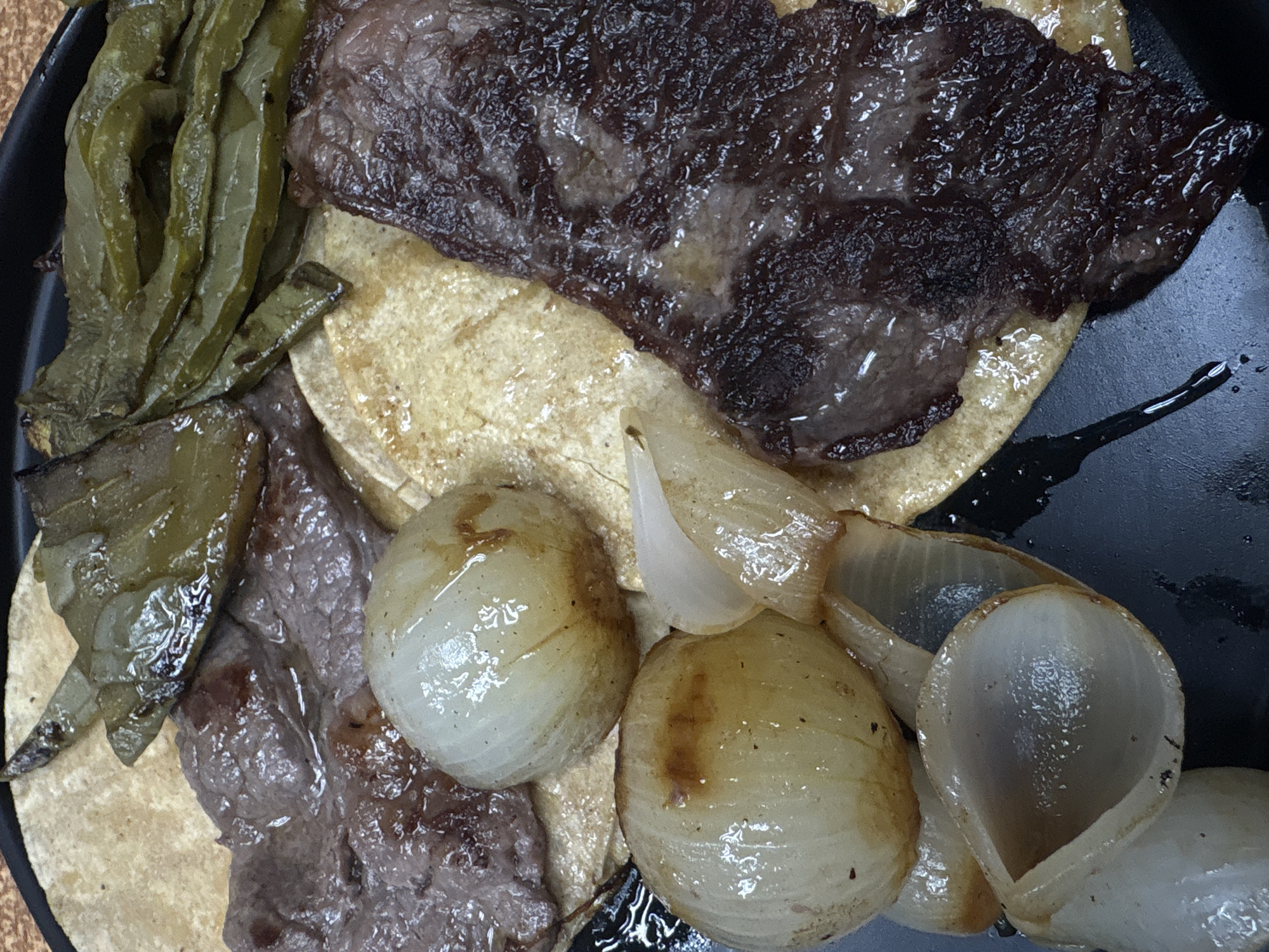 The image shows a plate of what appears to be tacos, possibly located in Mexico City, Mexico. The plate contains tortillas topped with grilled steak, nopales (cactus paddles), and grilled onions. The steak pieces vary in size and are slightly charred. The nopales are cooked and have a soft texture. The onions are caramelized and have been sliced. The presentation is casual and appears to be a traditional Mexican dish. The plate is black and some oil or grease is visible on the surface.
