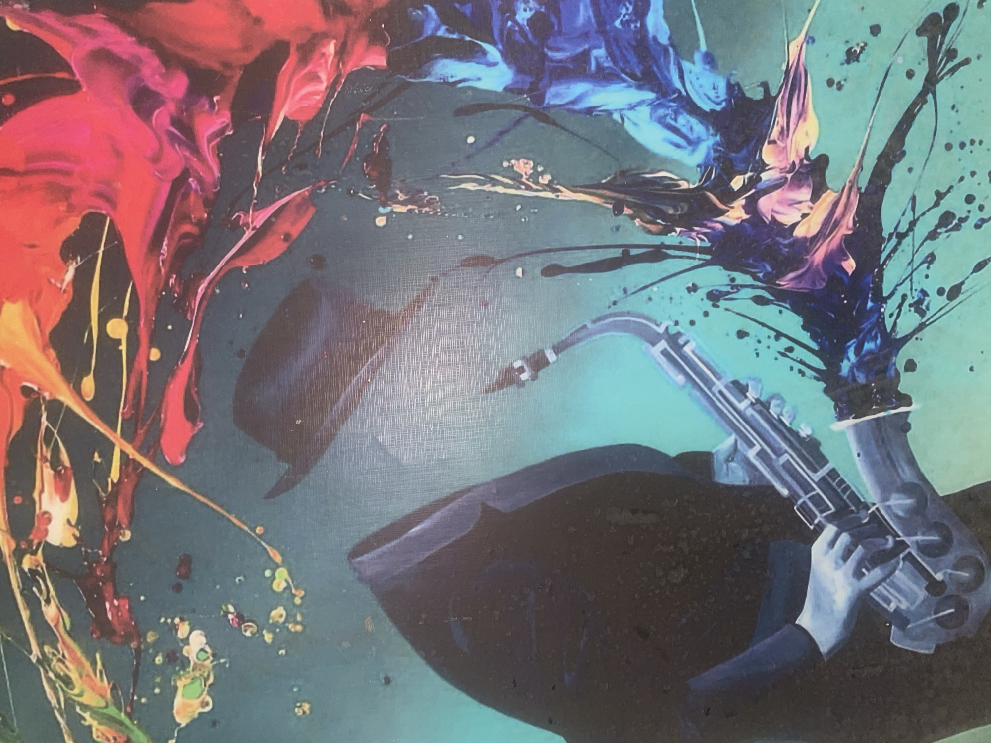 The image depicts an abstract painting featuring a jazz musician playing a saxophone. The musician, clad in a dark suit and hat, is rendered in cool blues and grays. The saxophone is silver. Swirls of brightly colored paint, including reds, oranges, blues, and purples, explode around the figure. The background is a teal color with splatters of various colors. The style is reminiscent of abstract expressionism. There is no indication this image is located in Abuja, Nigeria.