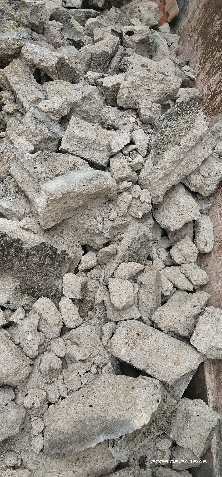 The image shows a pile of broken concrete pieces. The concrete is light gray and has a rough texture. Some pieces are large and blocky, while others are smaller and more irregular. The pile appears to be in a construction or demolition site. The background is a reddish-brown surface, possibly a wall or container, with some brickwork visible at the top right. A timestamp "2026.08.24 16:46" is present in the bottom right corner of the image, indicating the date and time the photo was taken. This scene is located in the city of Matabu, Indonesia.