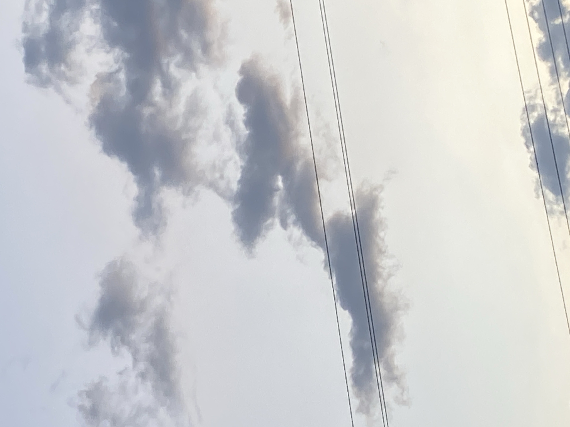 The image shows a view of the sky in Tinaquillo, Venezuela, with several gray clouds and overhead power lines.