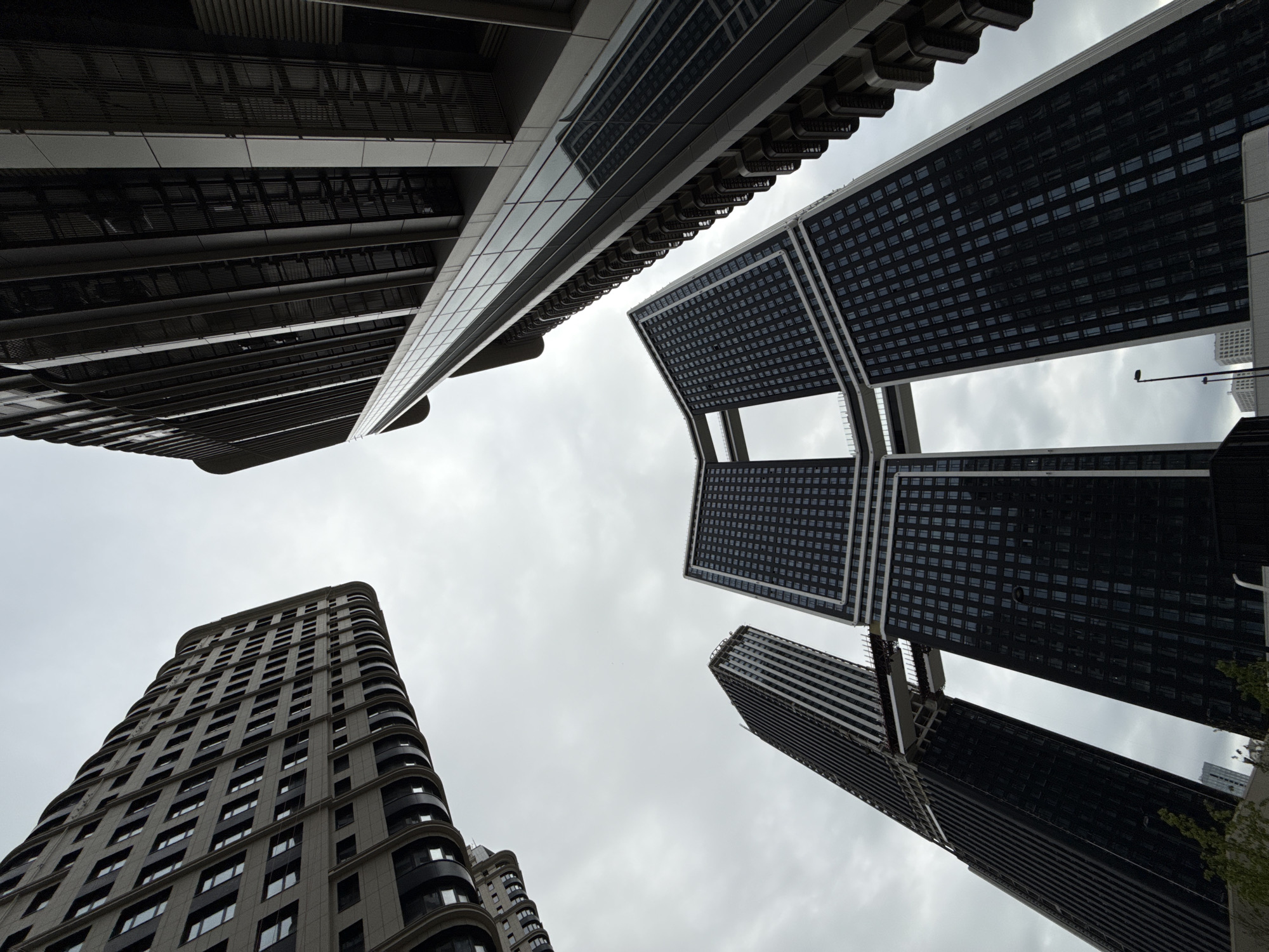 The image shows a low-angle view of several tall buildings against a cloudy sky. The buildings have varying designs and are made of materials such as glass, metal, and concrete. The architectural styles are modern, with some buildings featuring unique designs such as connecting sections in the upper floors. The scene's location in Khimki, Russia, cannot be confirmed from the image alone.