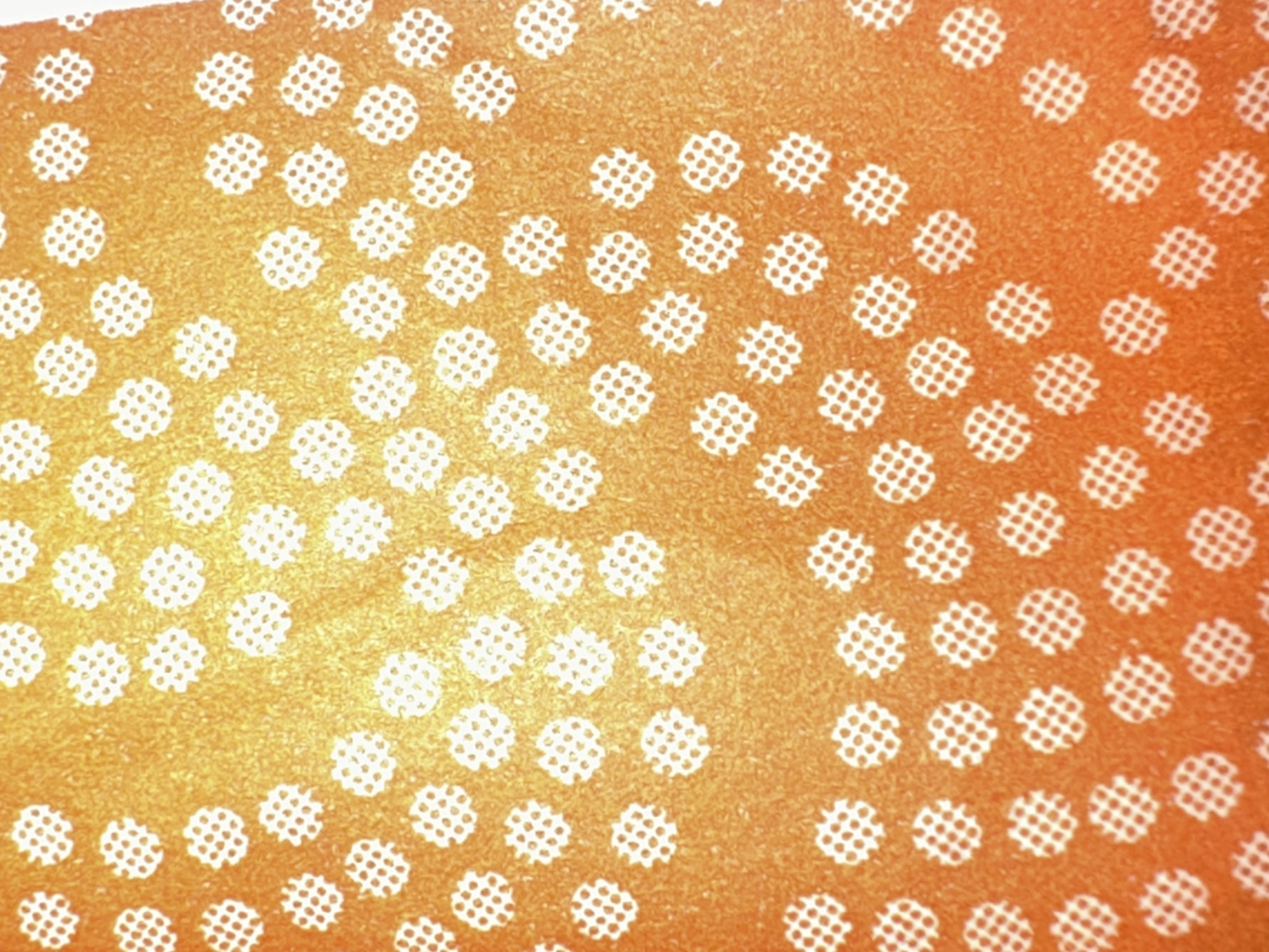 The image is a close-up, top-down view of an orange surface with a repeating pattern of small white circular shapes. Each white circle contains a grid of smaller dots. The orange surface has a slightly textured, gradient appearance, transitioning from a brighter yellow-orange in the upper left to a deeper orange towards the bottom right. This image does not contain any information that would allow for the identification of a specific location in Letterkenny, Ireland, nor does it depict any people, actions, or interactions.