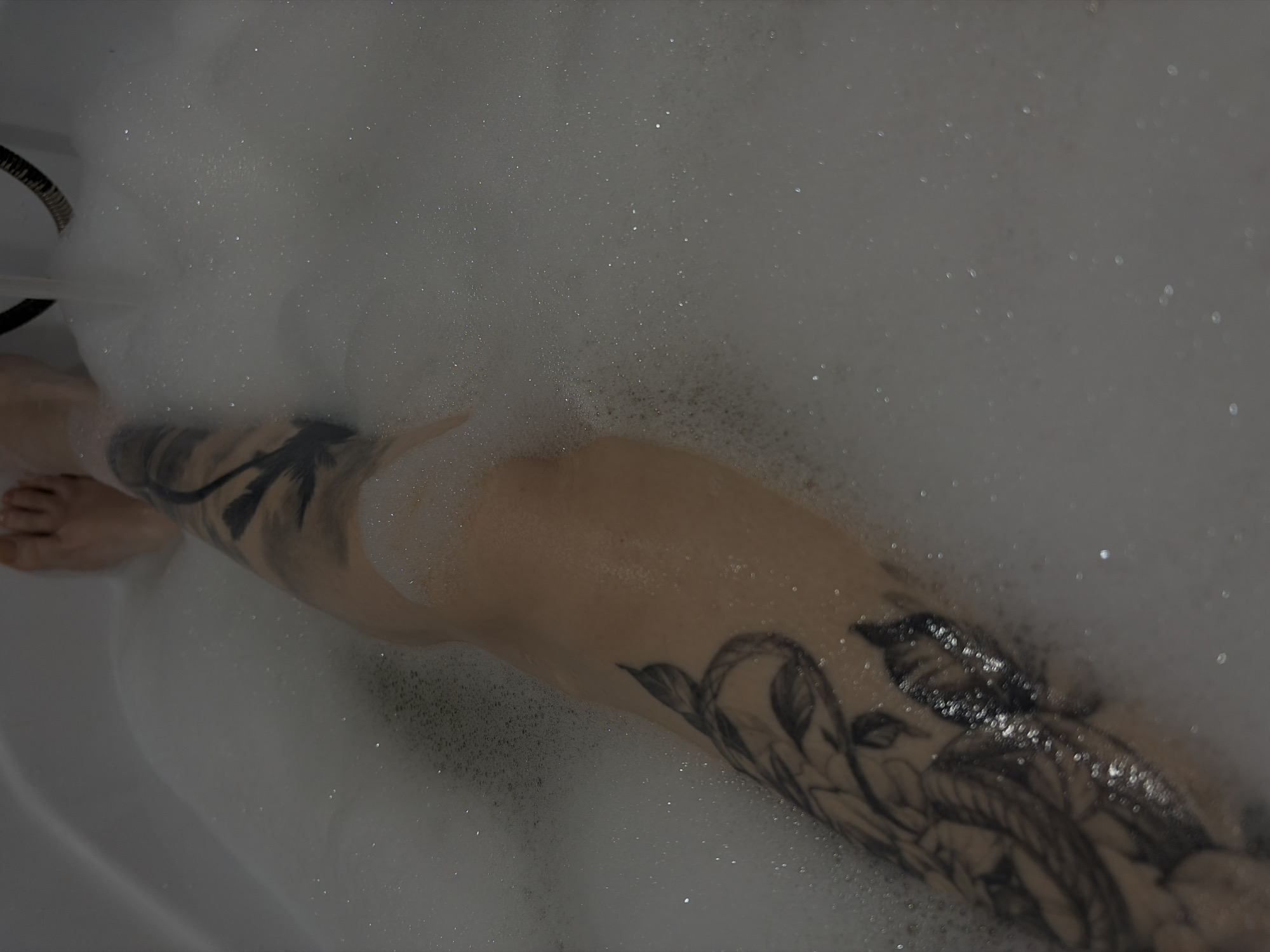 The image shows a person in a bubble bath. Their legs are visible and have tattoos. The setting appears to be a bathroom. The location in the city of Chaikovsky, Russia cannot be confirmed.