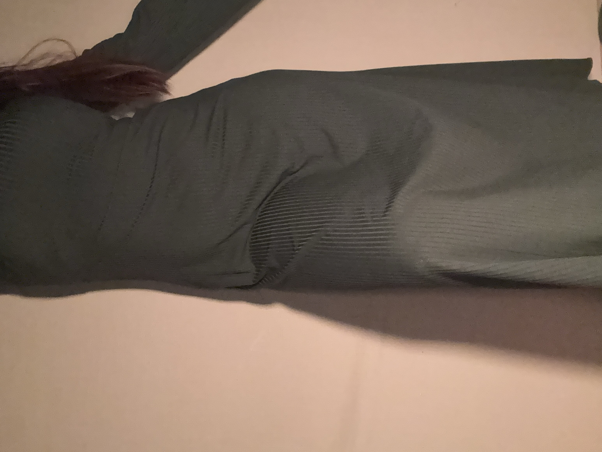 A person wearing a long-sleeved, dark green, ribbed garment is lying on a light tan or beige surface. Part of their dark brown or auburn hair is visible near the top left corner. The surface appears flat and featureless. The scene is indoors, with minimal visible context. There is no indication of location in Izhevsk, Russia or any other specific place.