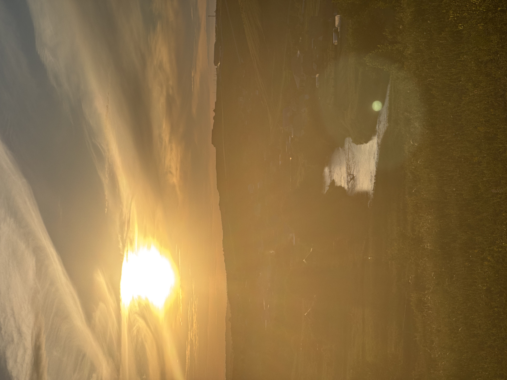 This media file depicts a picturesque sunset over a tranquil natural setting in Baiki, Russia. The scene is dominated by the vibrant hues of the setting sun, casting a warm, golden glow across the sky and land. wispy clouds stretch across the sky, catching the light and adding depth to the atmospheric display.
The landscape features a body of water reflecting the brilliant sky, possibly a river or lake, with a grassy embankment lining one side. In the distance, a cluster of structures suggests a small settlement or rural area, with a few faint outlines of buildings and possibly some trees. The overall impression is one of peace and natural beauty, enhanced by the soft, diffused light of the sunset. There are no visible people or explicit activities taking place, allowing the focus to remain on the serene landscape and the dramatic sky.
The time of day is clearly sunset, characterized by the low angle of the sun and the warm, orange and yellow tones. The weather appears calm, with no indications of wind or rain. The location cues, such as the architectural style of the distant structures and the type of vegetation, combined with the provided location context of Baiki, Russia, help to ground the scene in a specific geographical area. The overall emotion evoked is one of serenity and awe inspired by the natural spectacle. No visible text is present in the image.
