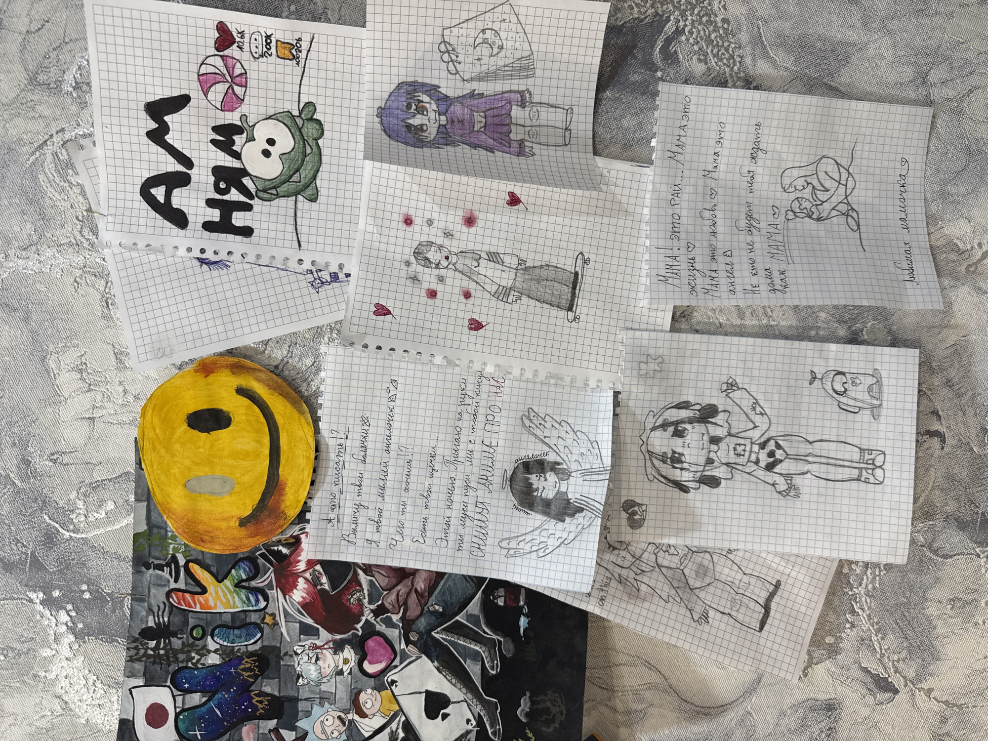 The image shows a collection of sketches and handwritten notes on graph paper scattered on a textured surface. The drawings include cartoon characters, anime-style figures, and doodles. One note is dedicated to "MAMA" and expresses love and admiration. Another contains playful writing and mentions "anime." A yellow smiley face sticker and other stickers featuring cartoons and symbols are also visible. The location is unknown, and there is no information indicating Rusanovo, Russia.