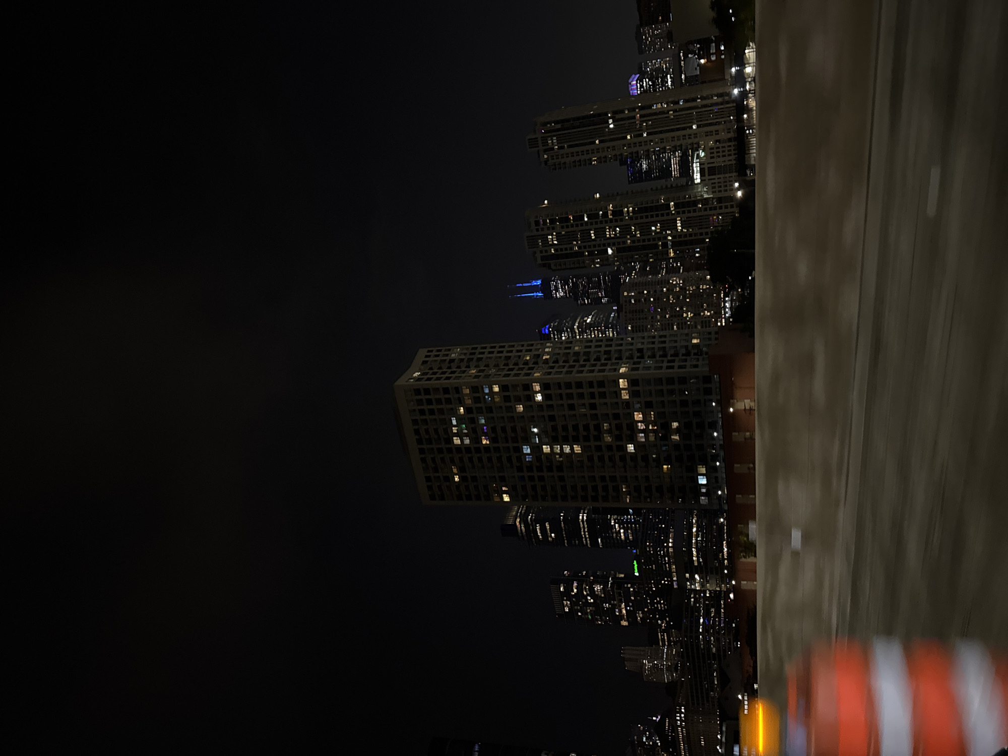 View of the city of Chicago at night. The buildings and city lights illuminate the dark sky. Construction cones are in the bottom right.