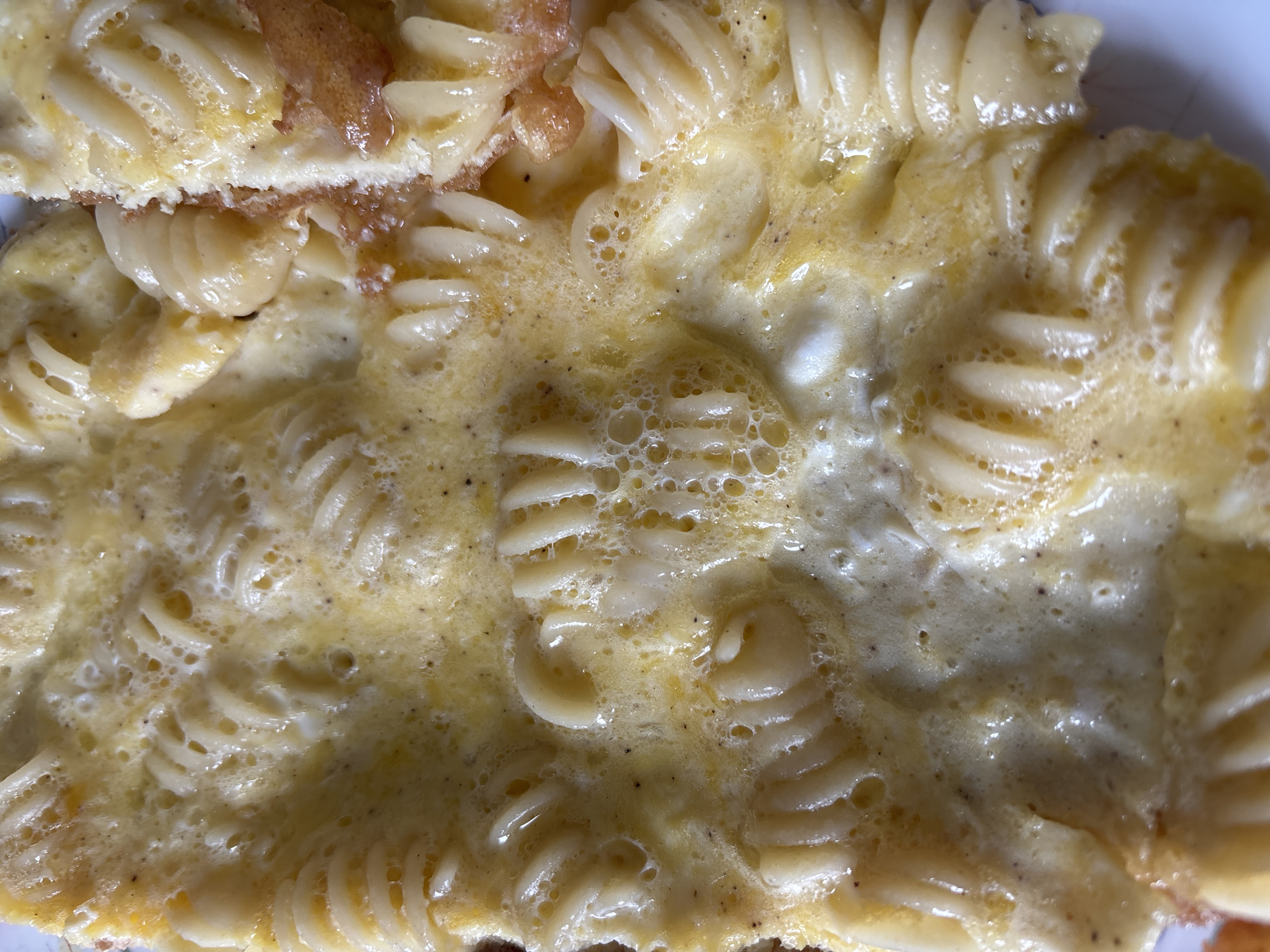 The image is a close-up, overhead shot of fusilli pasta cooked with scrambled eggs. The pasta spirals are clearly visible, coated and interspersed with the cooked egg mixture, which has a slightly bubbly texture in places. Some small dark specks, likely pepper or herbs, are scattered throughout the egg. The lighting is bright, highlighting the sheen of the food. There are no discernible elements of the city of Bila Tserkva, Ukraine, in the image.