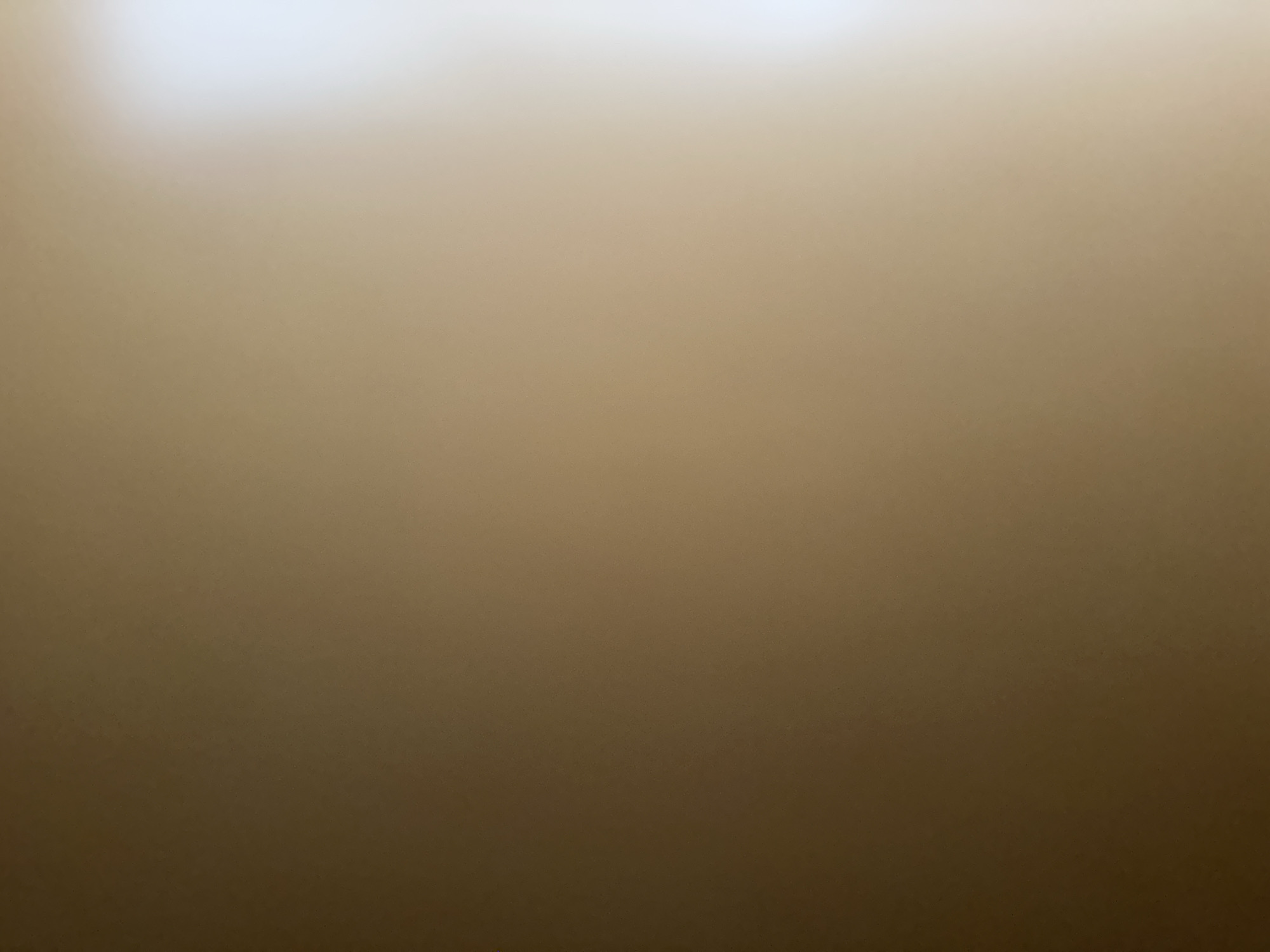 The image is an abstract, out-of-focus shot of a wall with a gradient of light and shadow. The left side of the image is darker, a deep brown, while the right side is significantly lighter, transitioning to a bright white due to an unseen light source. There are no discernible objects, people, or actions in the image. The overall impression is that of a textured surface, possibly a painted wall, illuminated from the right. The location in Belgrade, Serbia, cannot be determined from the visual information provided.