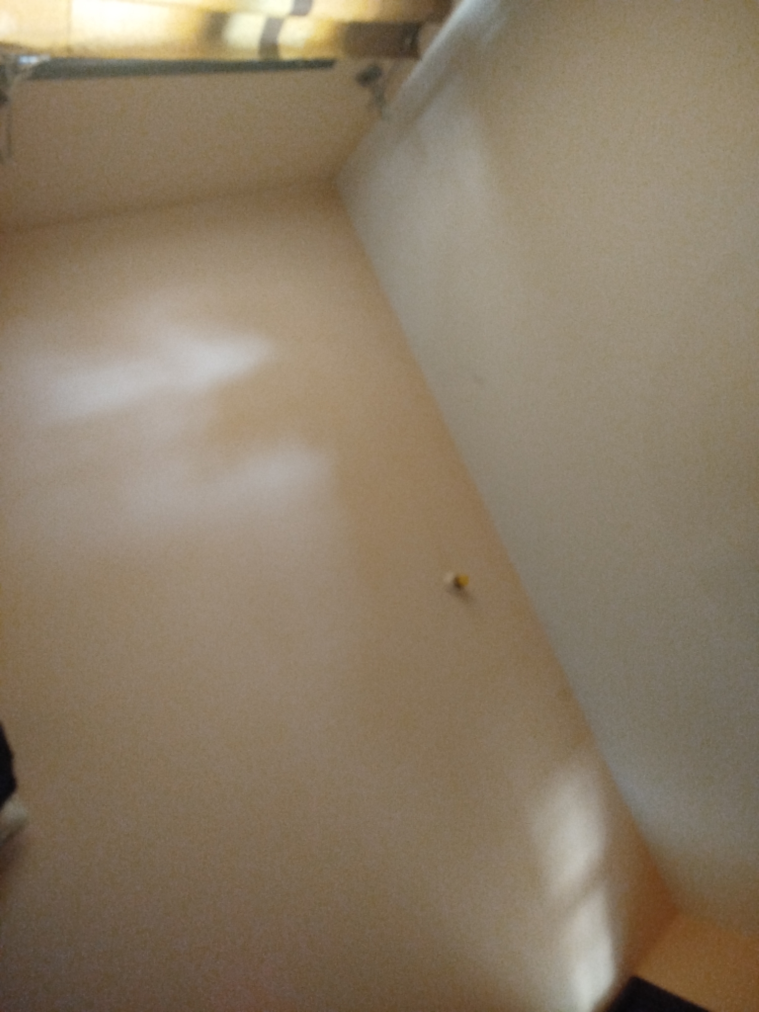 The image shows an interior of a room with light-colored walls. The room appears empty, with no furniture or significant objects visible except for a small yellow thumbtack or pin on the right wall. There is a light source coming from the upper left corner, casting some shadows on the wall. The overall impression is of a plain and sparsely decorated space. The provided crops offer slightly closer views of different sections of the wall and the upper corner. No specific details related to Lassan, Pakistan are discernible from the image itself.