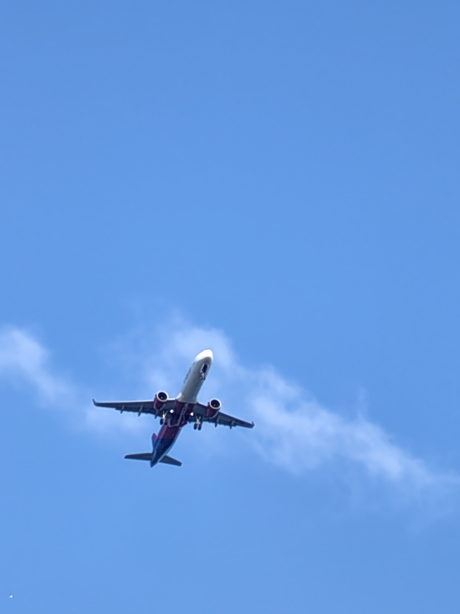 The image shows an airplane in the sky. The plane has a white fuselage and red and blue wings and tail. The sky is blue with a few scattered clouds. The location in Varna, Bulgaria is not verifiable from the information in the image.