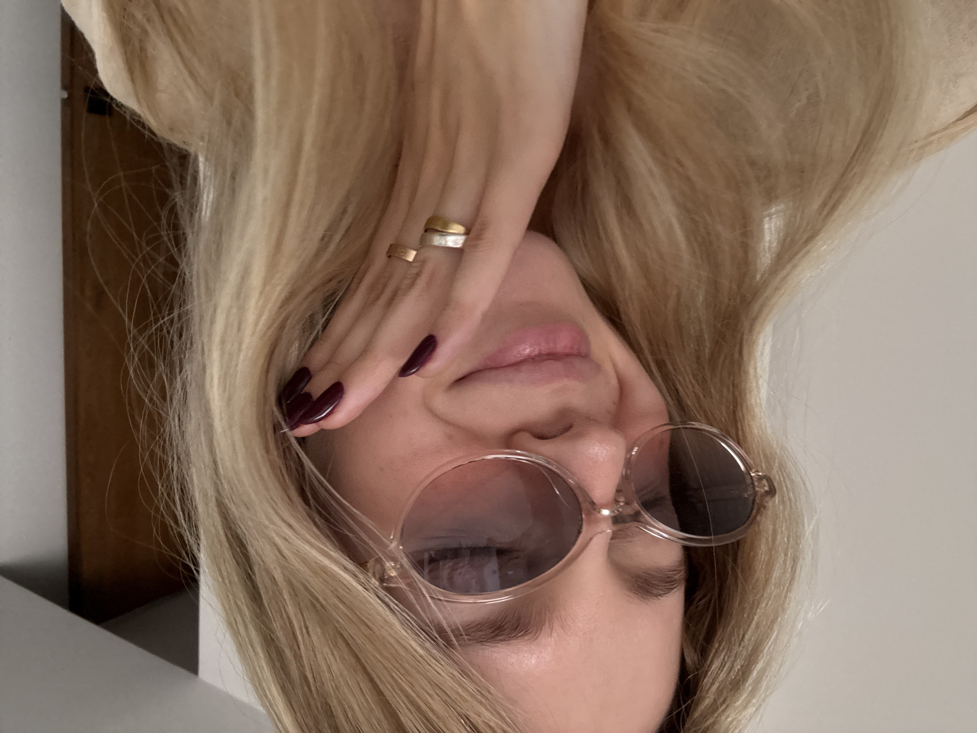 A light-skinned woman with blonde hair is pictured from an upside-down perspective. She is wearing round, tinted sunglasses and has two rings on her finger. Her fingernails are painted in a dark color. The location, Mexico City, Mexico, is not discernible from the provided image.