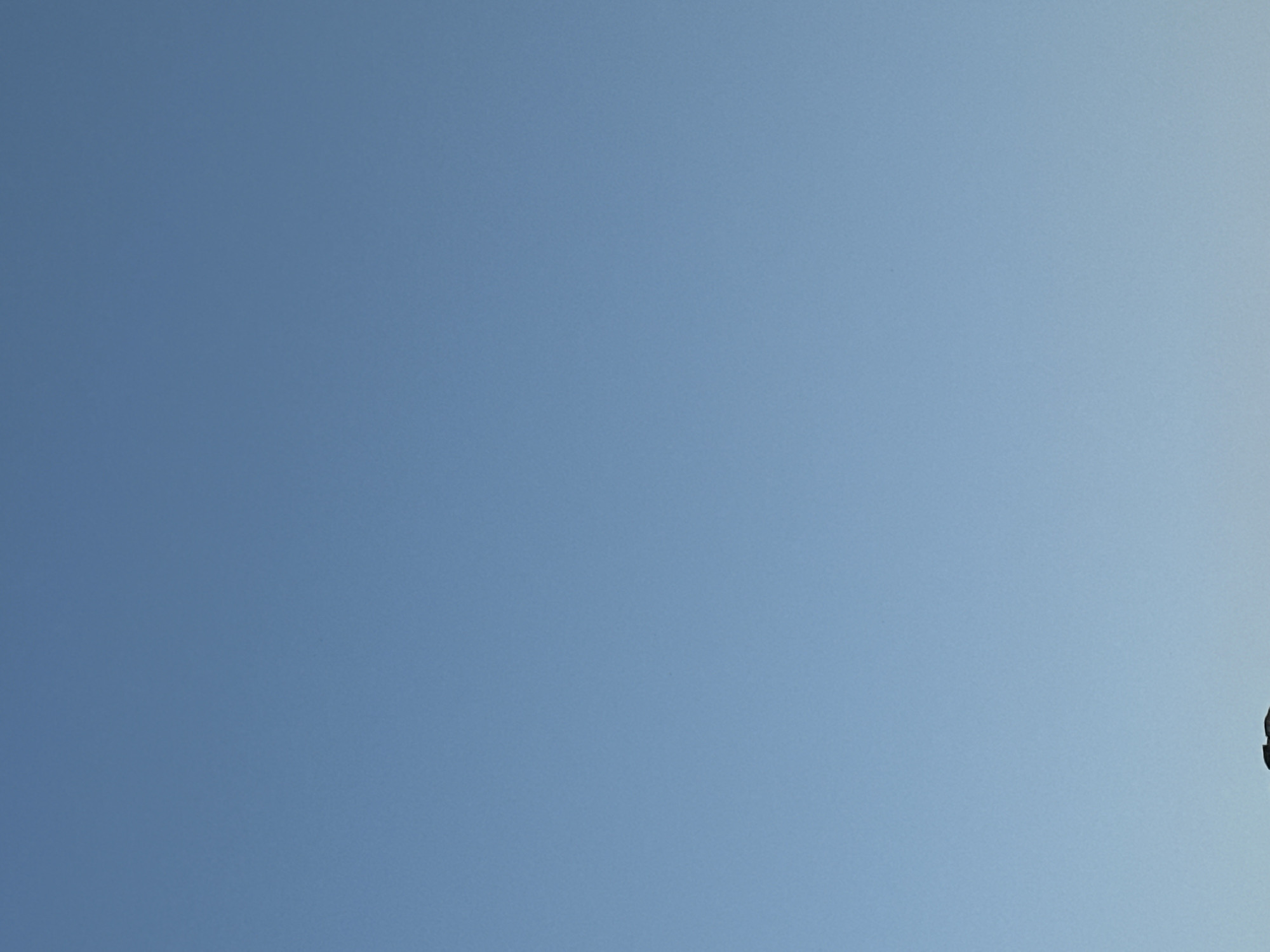 The image shows a clear, pale blue sky with a dark, silhouetted object at the very bottom edge. The object appears to be a flat surface with some irregular protrusions, possibly the top of a building or structure, or a natural land formation. No specific details about the location in Tobyl, Kazakhstan, can be discerned from the sky alone.
