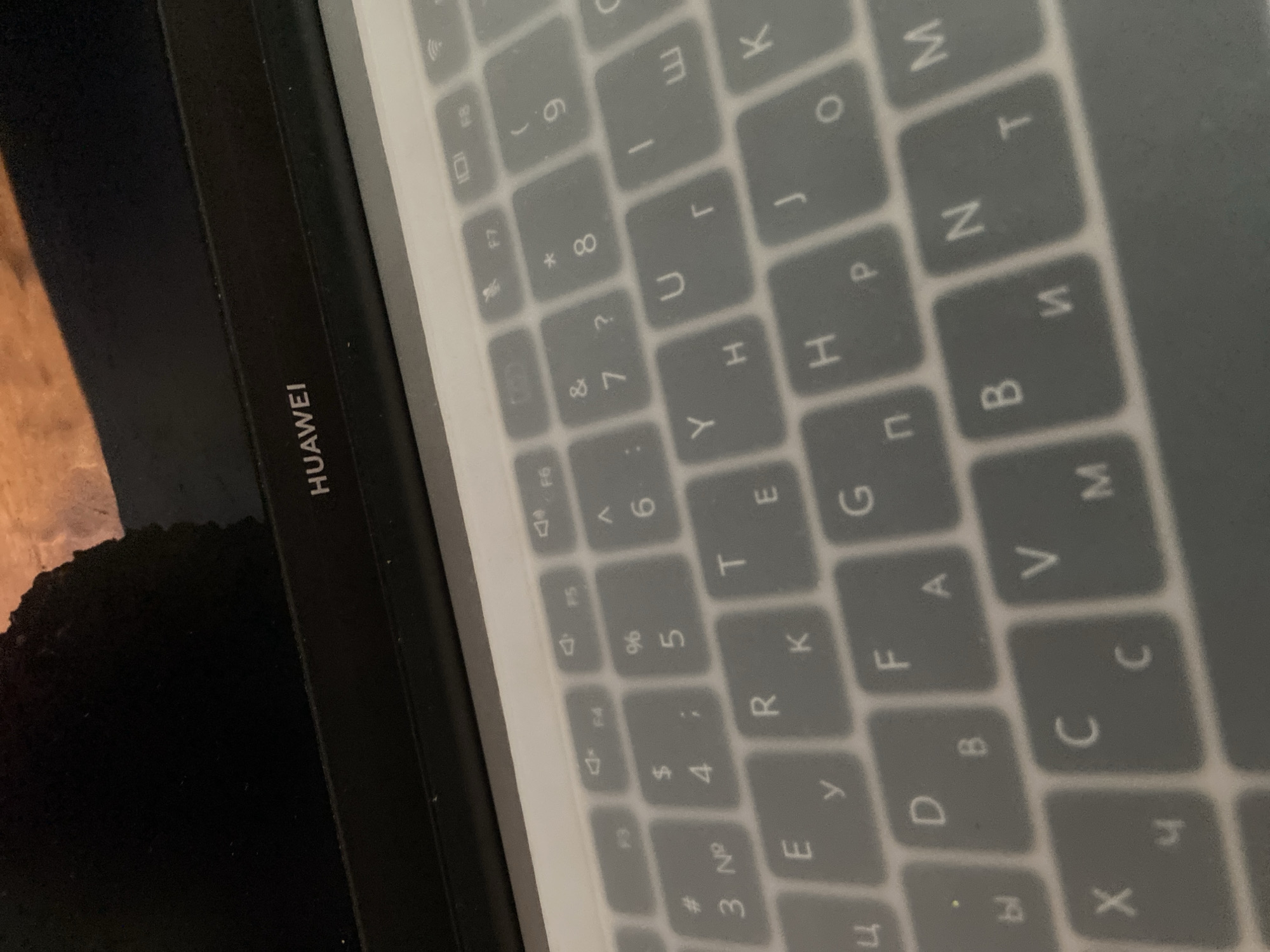 The image shows a close-up view of a laptop keyboard with a clear protective cover. The "HUAWEI" logo is visible on the bezel above the keyboard. The keys are gray with white characters, some of which appear to be Cyrillic letters. The lighting suggests an indoor environment, possibly a desk or workspace. No specific location in a city is identifiable from the image.