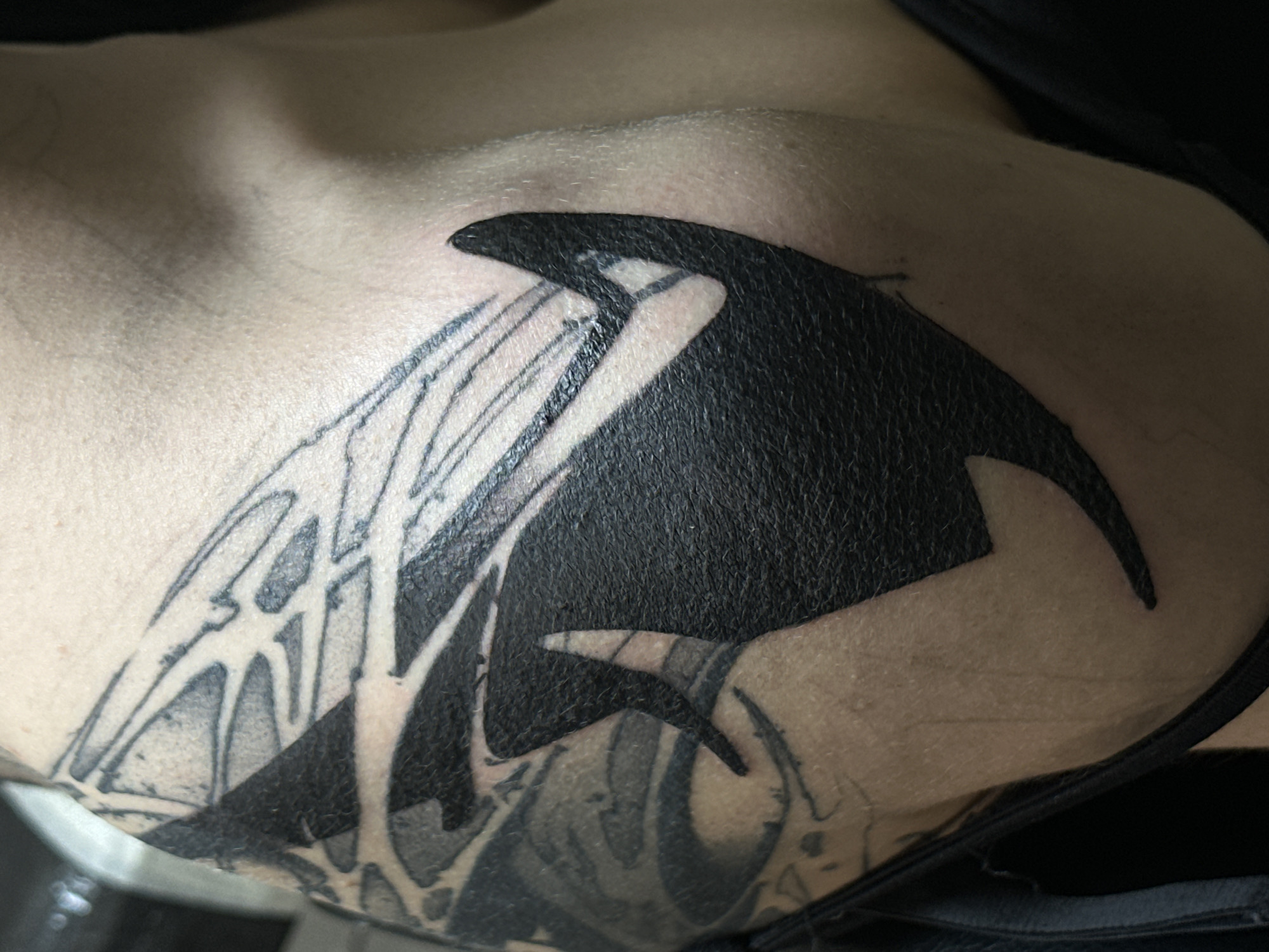 Close-up photograph of a tattoo on a person's upper chest/shoulder area. The tattoo features a large, solid black silhouette of an orca whale with geometric lines extending outward from its head and belly. There is pre-existing tattoo shading near the bottom of the image. The skin appears fair. The scene is indoors. Moscow, Russia, is not apparent in the image.