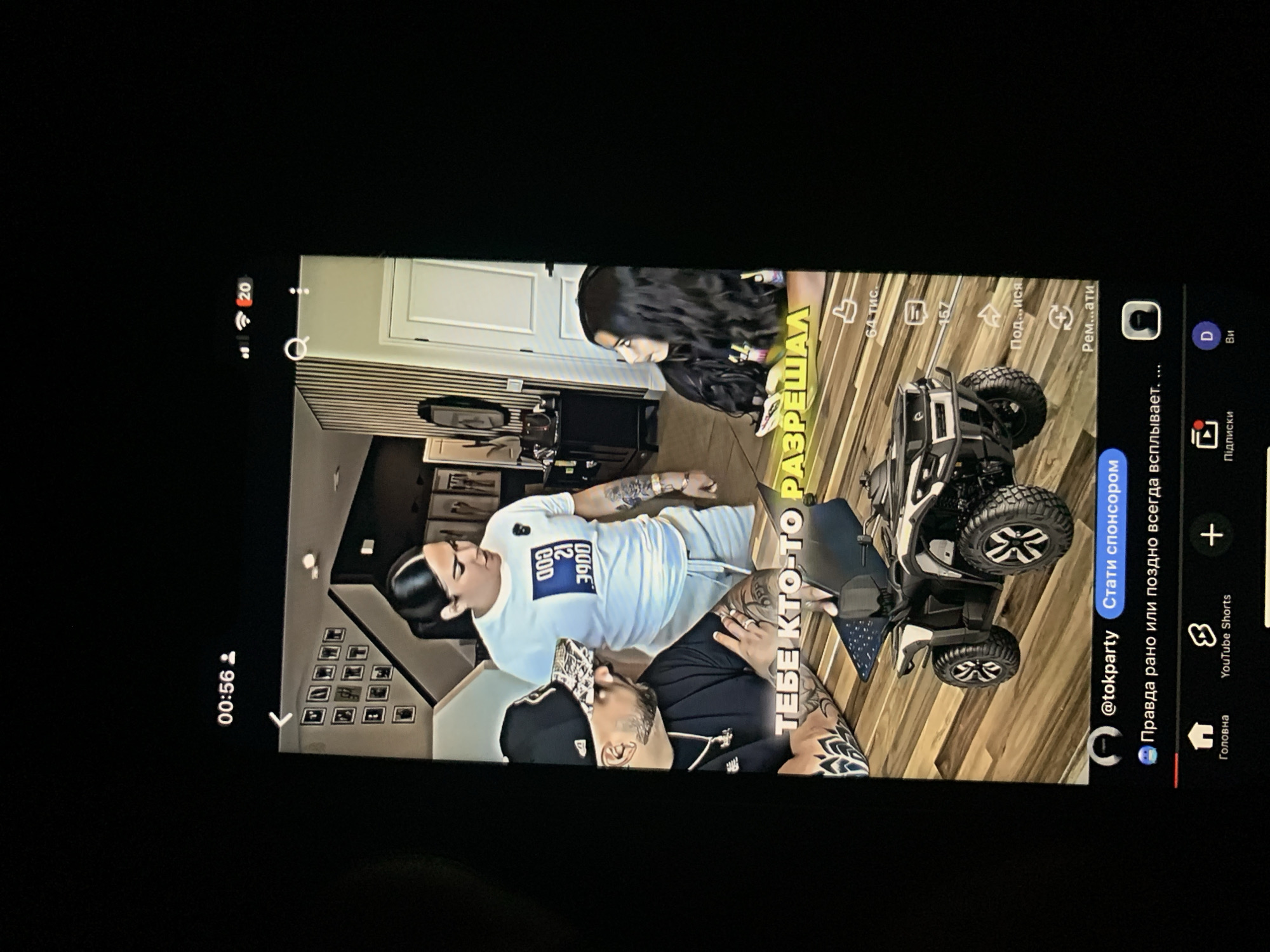 The image shows a TikTok video interface on a black screen. The video features three people and a toy ATV. In the foreground, a man wearing a black baseball cap and a black t-shirt is seated at a wooden table, looking at a laptop. He has tattoos on his arms. To his right, a woman in a white t-shirt with text and grey sweatpants stands and looks towards the man. Behind them, another woman with long dark hair is seated, looking to her right. A toy ATV is placed on the wooden floor in the center of the frame. The video has Russian text overlays, including "ТЕБЕ КТО-ТО РАЗРЕШАЛ" which translates to "Who gave you permission?". The bottom of the screen shows TikTok interface elements, including the username "@tokparty", a button for "Стати спонсором" (Become a sponsor), and navigation icons for "Головна" (Home), "YouTube Shorts", "Підписки" (Subscriptions), and "Ви" (You). The image does not provide any information about the city of Zhmerynka, Ukraine, or any geographical context within that city.
