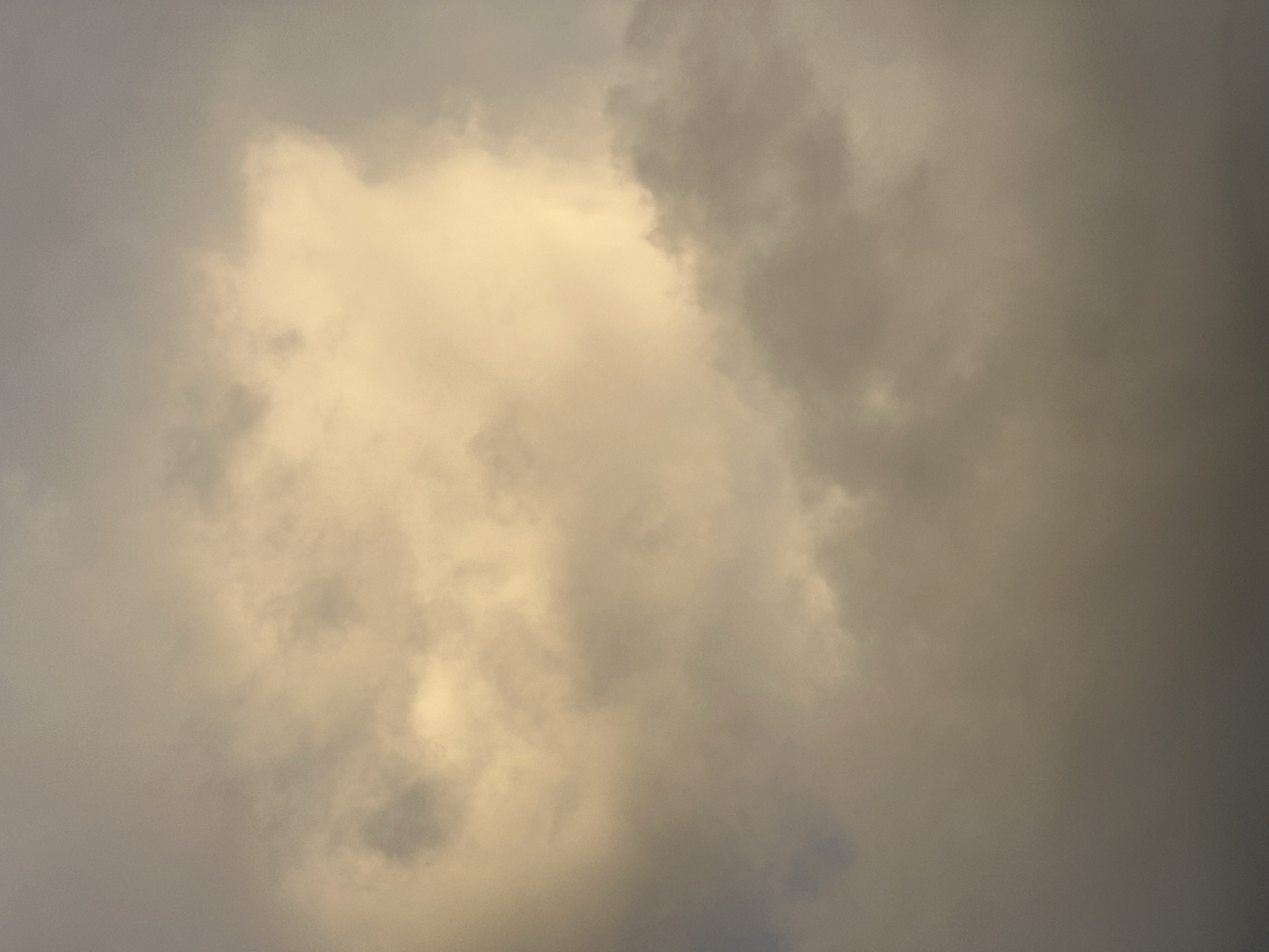 The image shows a cloudy sky. The color of the clouds ranges from light gray to dark gray, with a patch of lighter, almost yellow-toned clouds in the center. There are no people or objects visible other than the clouds. The location of the image is not discernible based on the provided information. There are no actions or interactions depicted in the image.