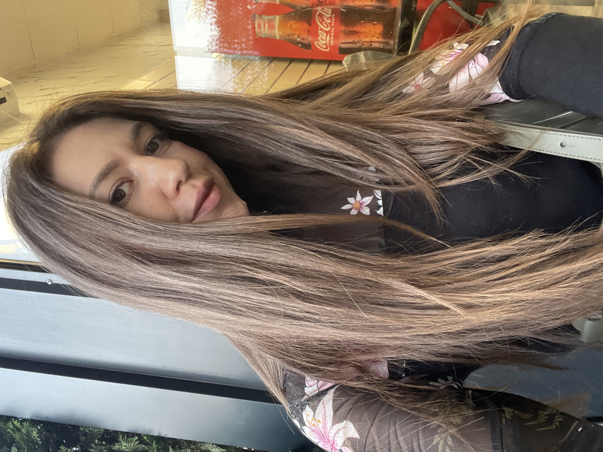 A woman with long brown hair is posing for a photograph. She's wearing a black top with floral embellishments. A Coca-Cola advertisement is visible in the background. The photograph appears to be taken indoors, possibly in a cafe or restaurant setting. It's not possible to confirm the location in Sofia, Bulgaria, without additional details or context.