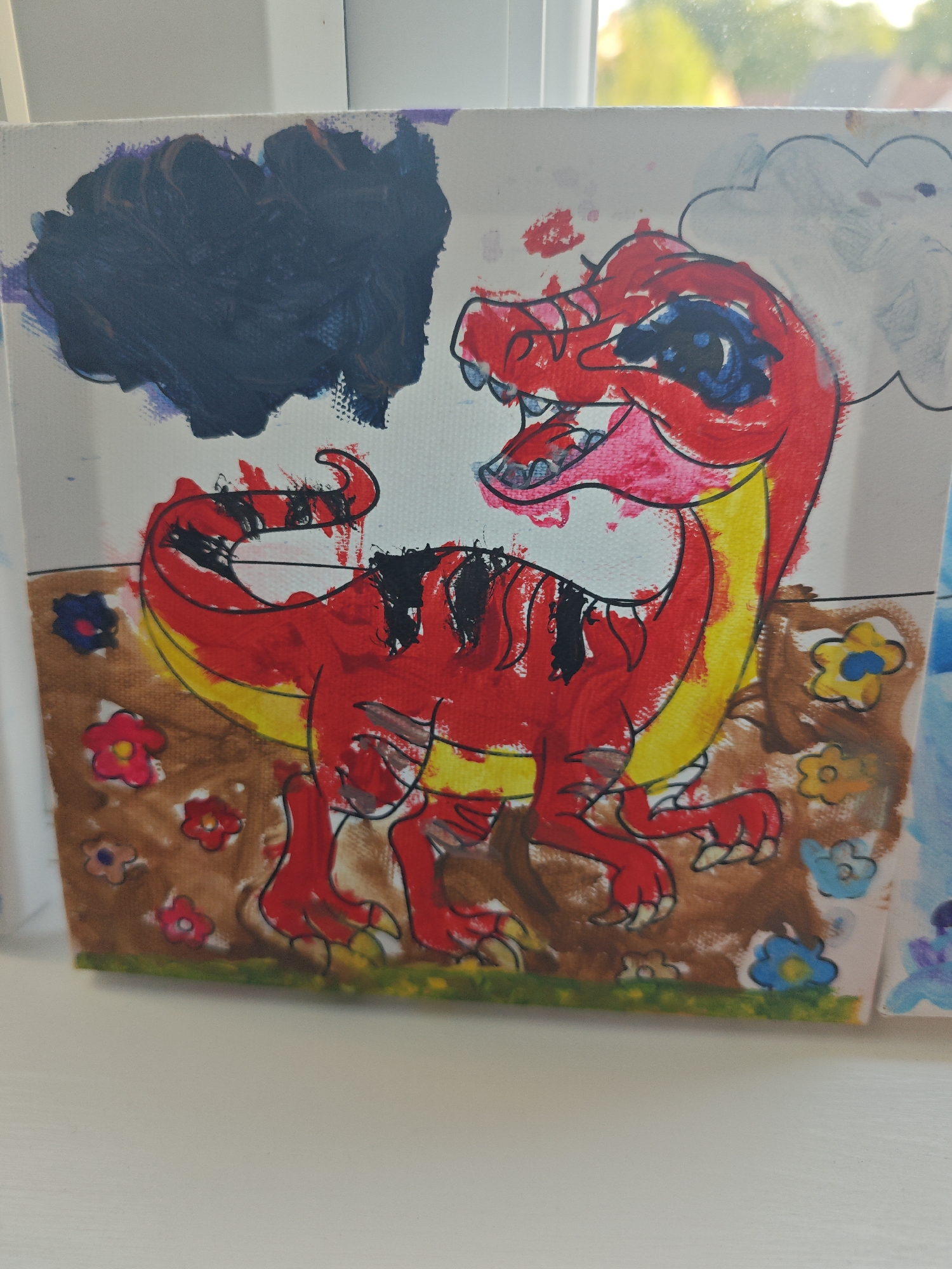 A painting on canvas depicts a red cartoon dinosaur with yellow accents on its neck and tail. The dinosaur is standing on brown ground dotted with colorful flowers. Above the dinosaur are dark blue and grey clouds. The painting is on a windowsill, with a blurred background of trees and buildings visible through the window. The location is Diss, United Kingdom.