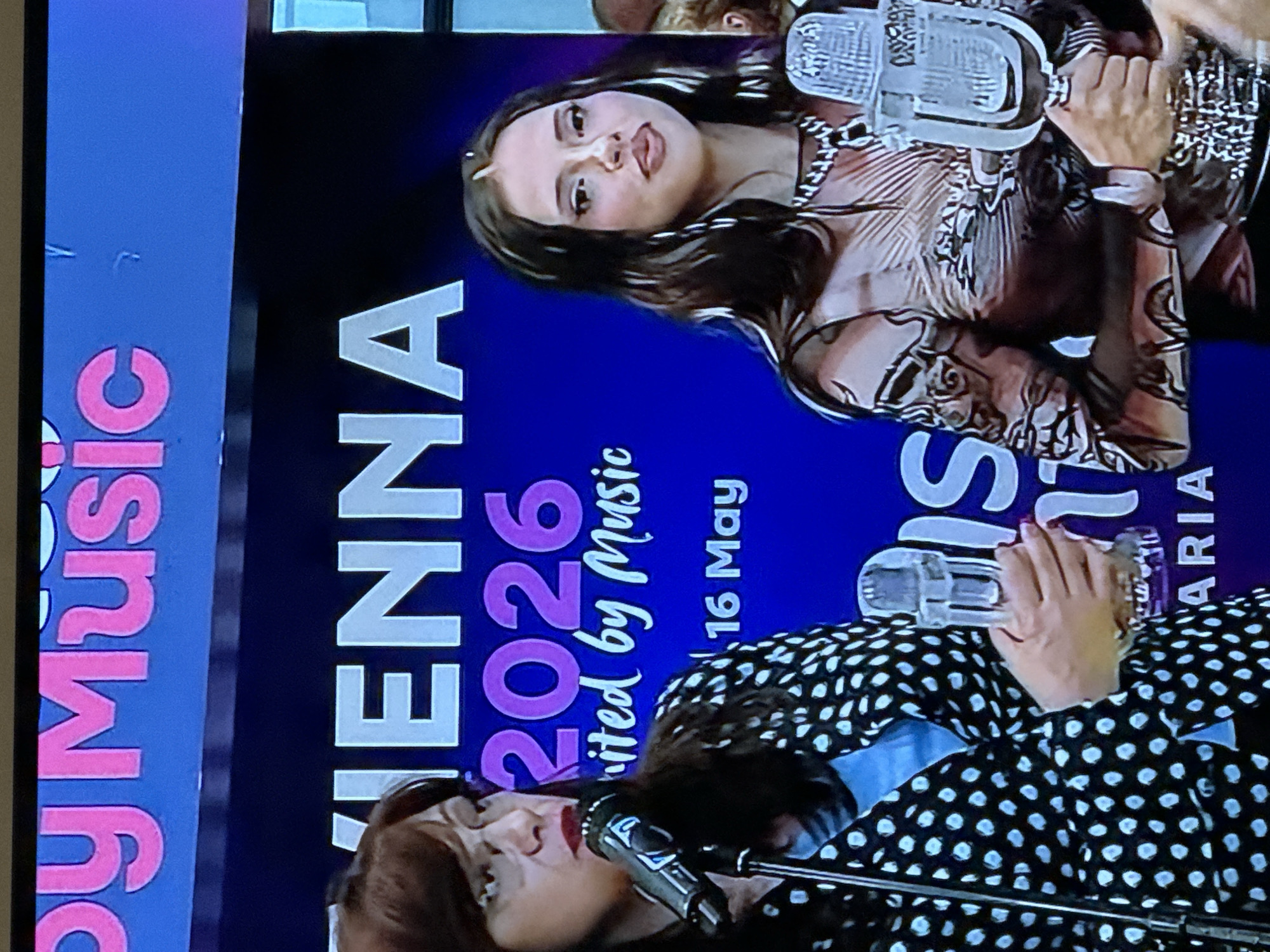 The image shows a promotional display for "Vienna 2026, United by Music, 16 May", alongside "byMusic". Two women are featured, one wearing a patterned top and another in polka dots, both with microphones. The location in Sofia, Bulgaria is not evident.