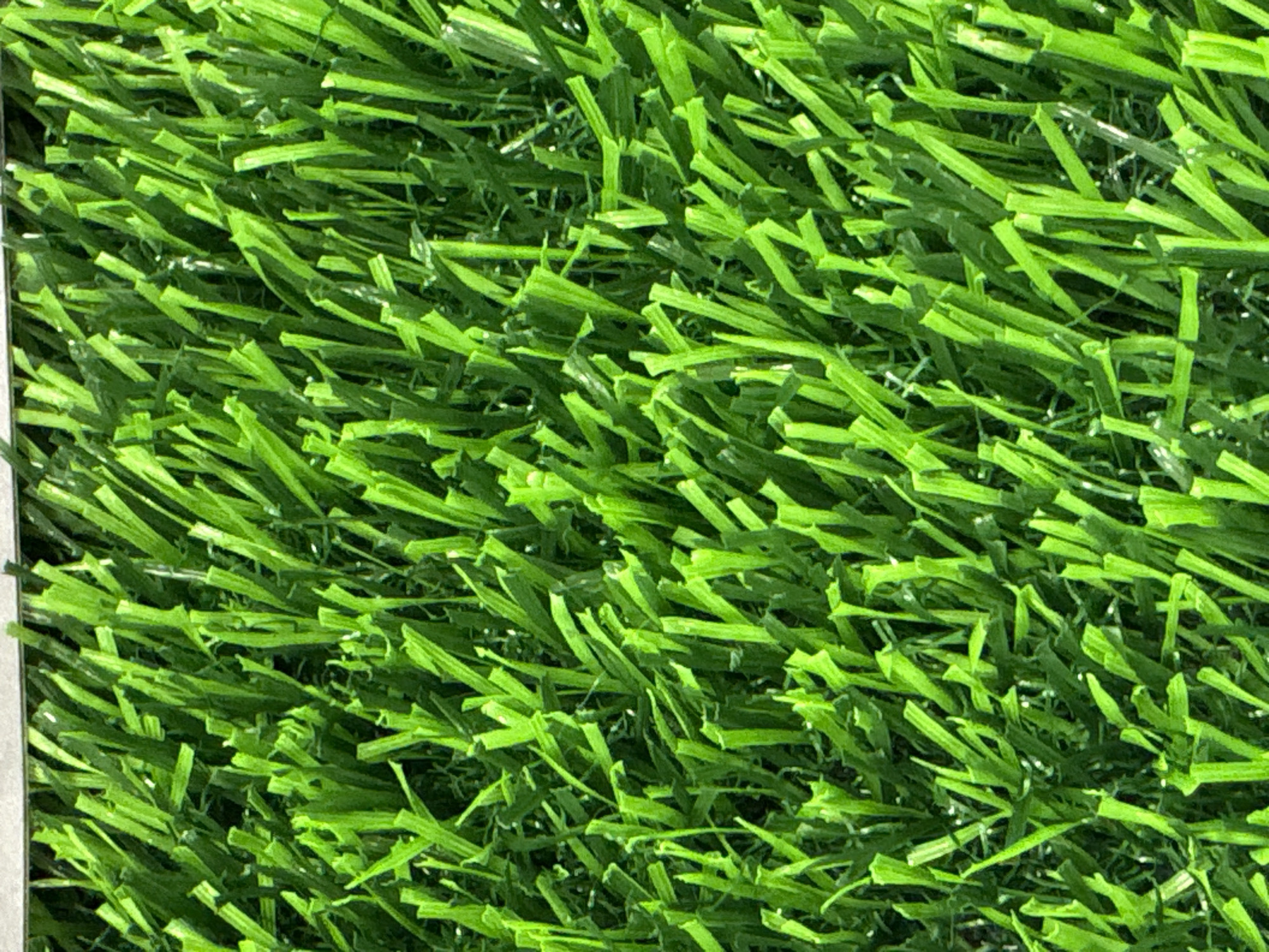 The image shows a close-up view of artificial turf. The turf blades are a bright green color and are cut short, giving the appearance of a well-maintained lawn. The texture of the turf is dense, with individual blades visible and overlapping. There is no indication of a specific location within Søborg, Denmark, or any people or actions. The scene is static and focuses solely on the material of the artificial turf.