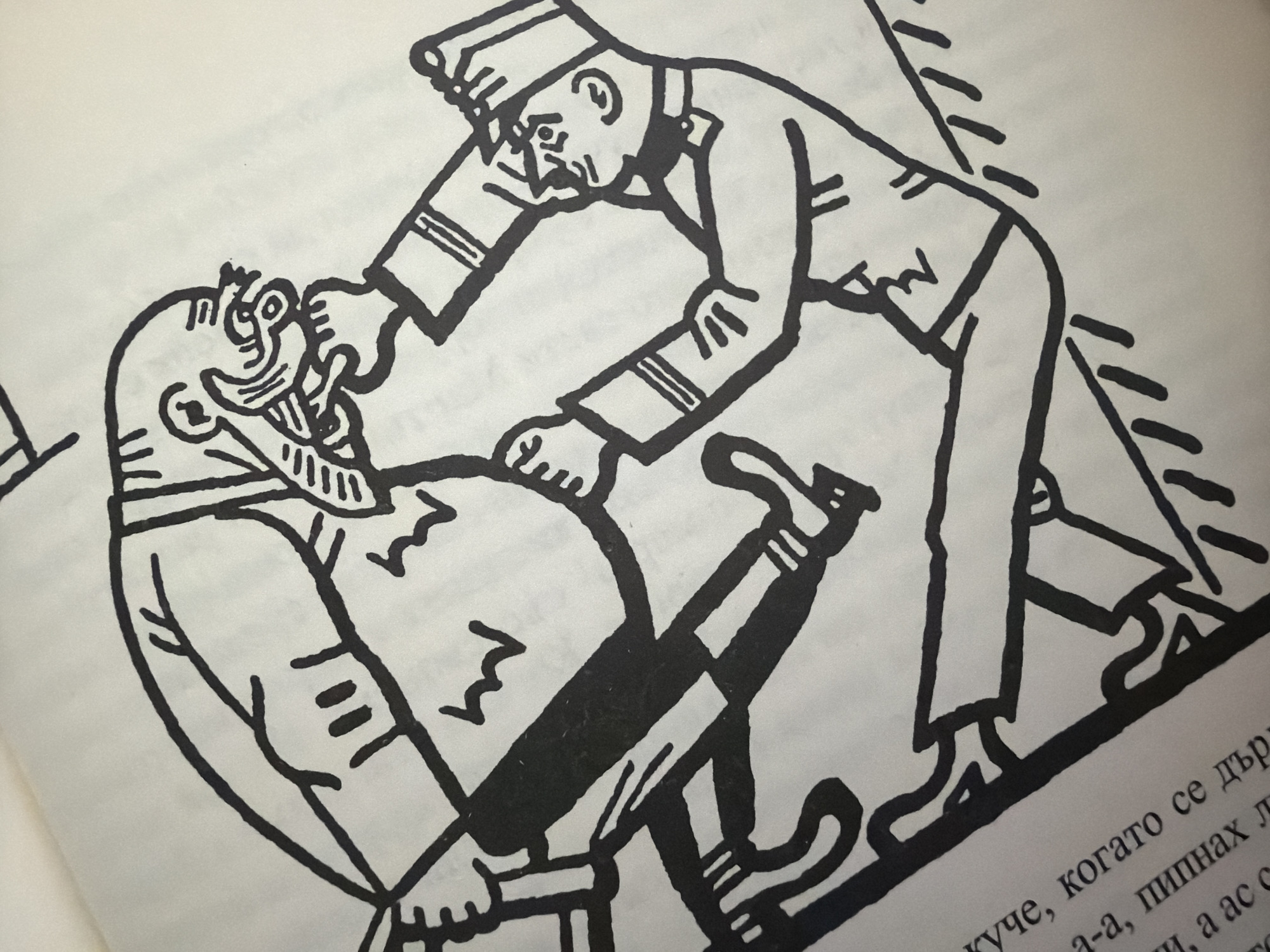 The image depicts a stylized black and white illustration of two figures interacting. One figure appears larger and more muscular, with a bald head and exaggerated facial features, including a prominent nose and mouth. This figure is holding the arm of the second figure. The second figure is smaller, wearing what appears to be a uniform with a cap, and is holding the first figure's arm. The illustration style is simplistic and bold, with thick black lines. The background is a plain, off-white surface. There is also text visible in the lower left corner of the image, written in Bulgarian Cyrillic script. The text is partially obscured but appears to be descriptive. The illustration does not contain any discernible elements that would place it in a specific city, including Pazardzhik, Bulgaria.