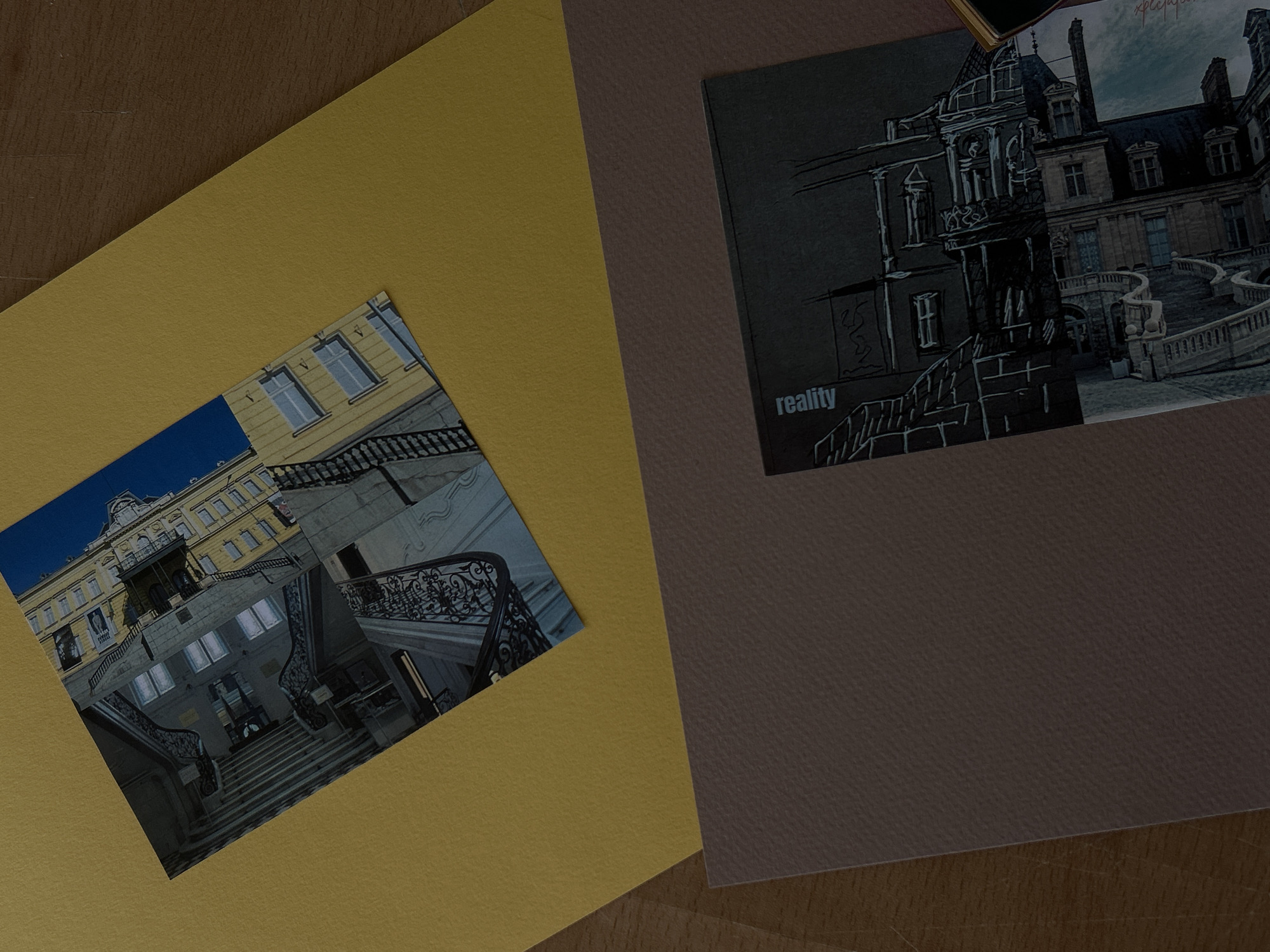 The image shows two postcards laid on textured paper. The top postcard features a building with yellow walls and ornate iron railings on a staircase. The bottom postcard displays a black and white sketch of a building with the word "reality" written vertically on the left side. The postcards are placed on a yellow sheet of paper, which is on top of a brown sheet of paper. The scene is set on a wooden surface. The postcards are not identifiable with any specific locations in the city of Sofia, Bulgaria.