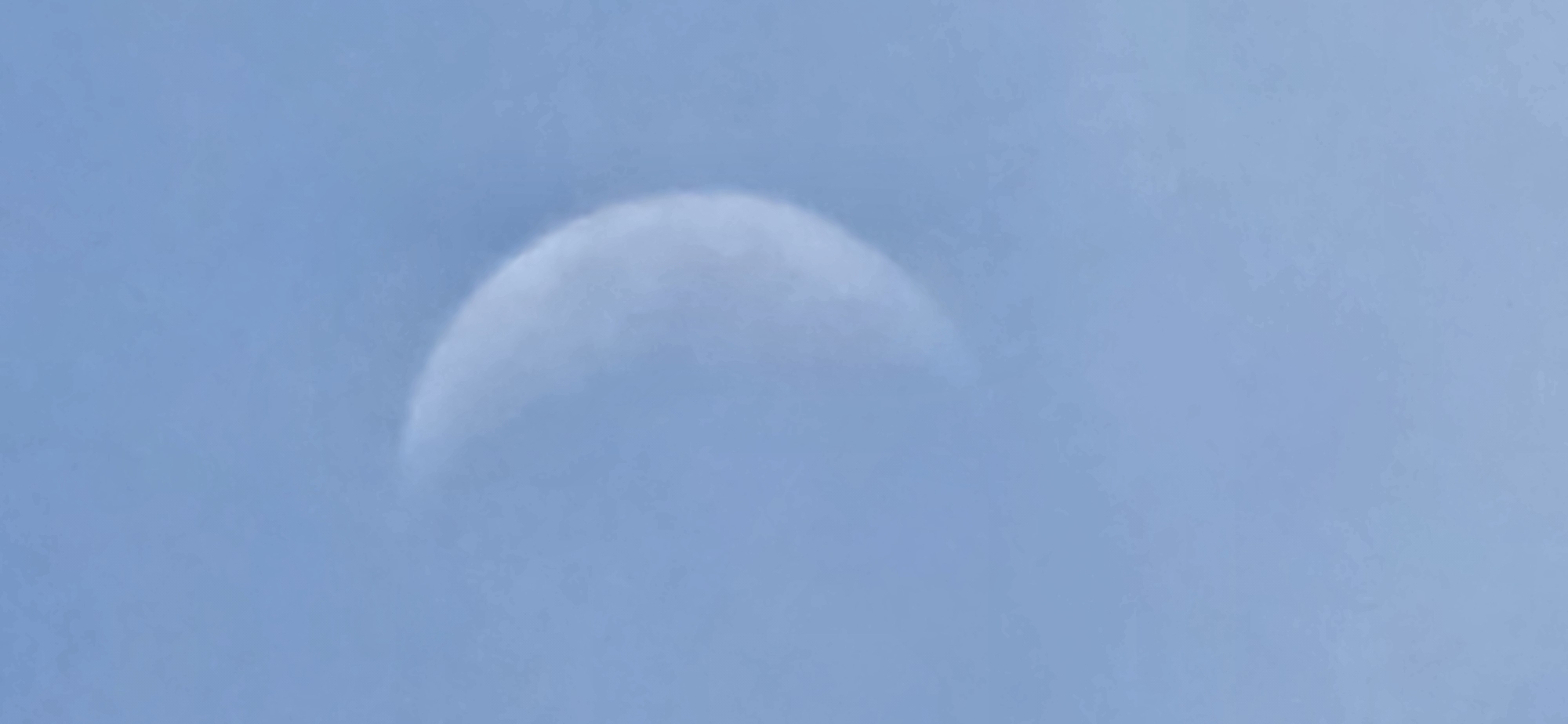 A crescent moon is visible in a pale blue sky, partially obscured by a thin layer of white clouds. The image was captured in Русская Деревня-2 Кп, Russia.
