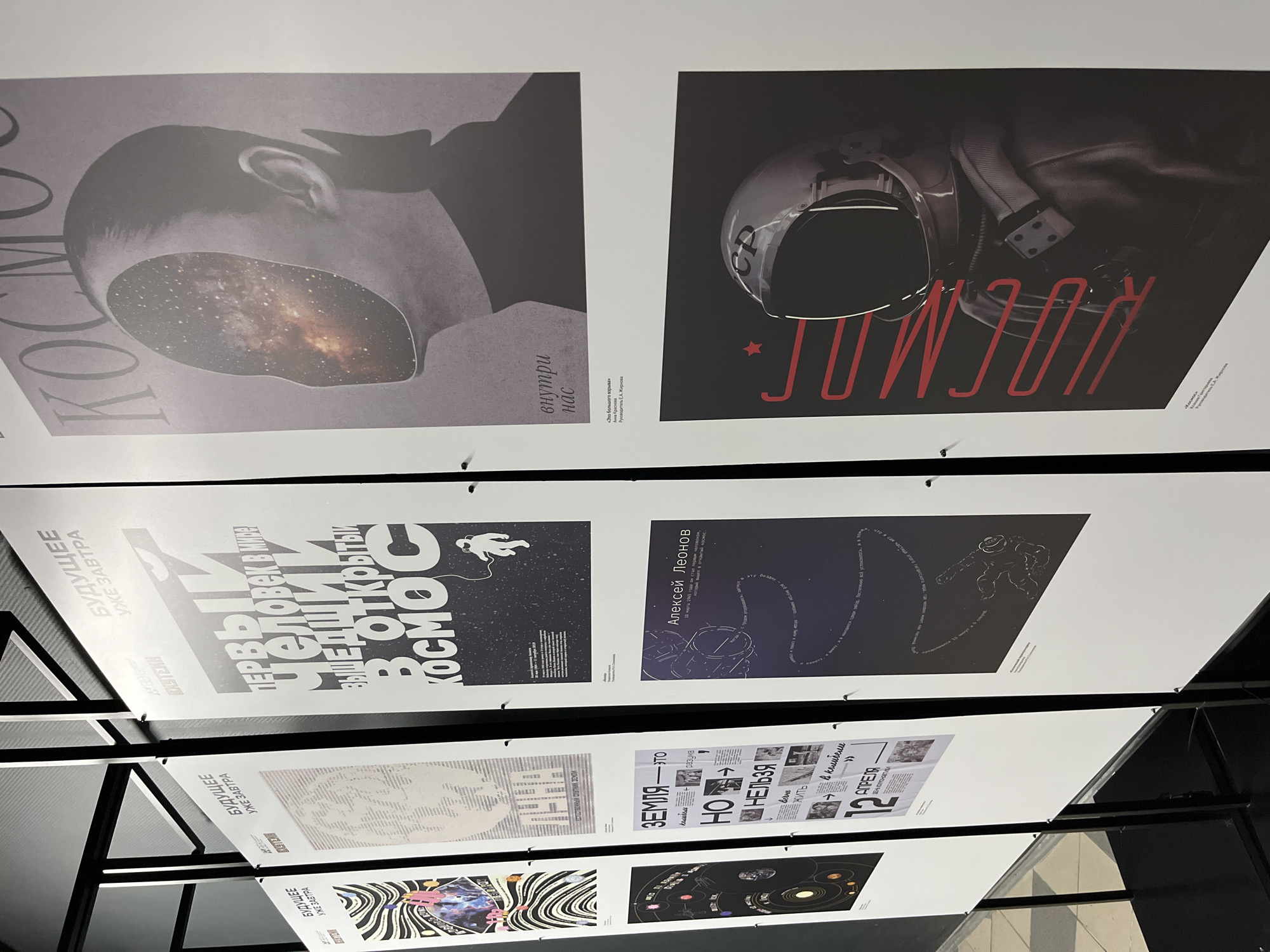 The image shows several posters displayed on a black metal frame. The posters feature space-related themes and designs. There is text in Russian on the posters. The location is a city named Unknown in Unknown.