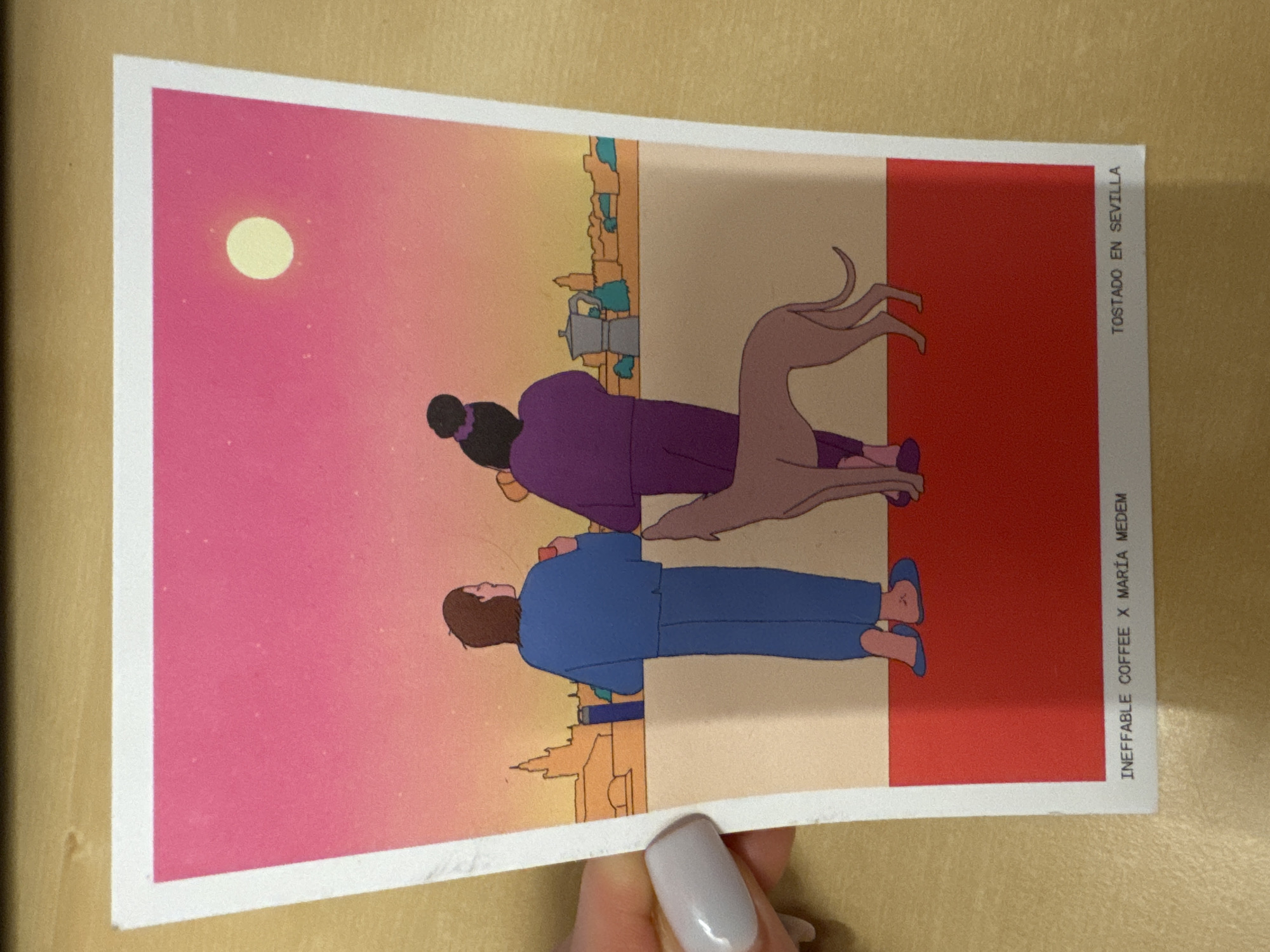 The image is a postcard featuring a colorful illustration of two people and a dog standing on a balcony overlooking a city skyline at sunset. The sky is a gradient of pink to orange, with a bright yellow circle representing the sun or moon. The two figures are depicted from behind, both holding cups, suggesting they are enjoying a drink. One person is wearing a blue outfit, and the other a purple outfit. A slender, light brown dog stands between them, looking towards the city. In the background, a cityscape is visible with buildings and a moka pot on the balcony railing. The postcard also has text at the bottom, "INEFFABLE COFFEE X MARÍA MEDEM" on the left and "TOSTADO EN SEVILLA" on the right. The image does not contain any information or visual cues to suggest a location in the city of Murcia, Spain.