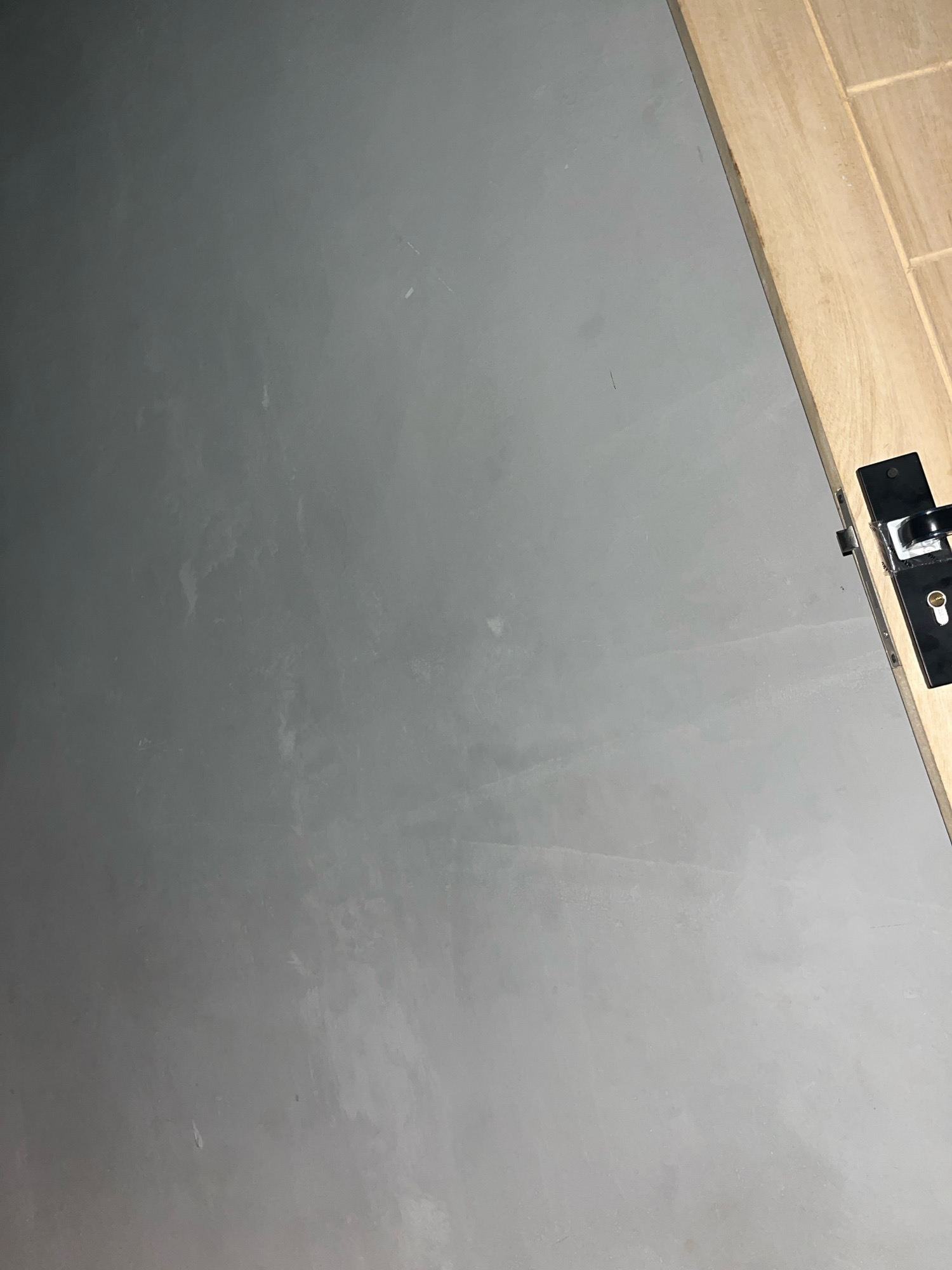 The image shows a close-up view of a gray, textured surface, possibly a wall or a door, with a light-colored wooden door frame on the right side. A black door handle with a keyhole is attached to the wooden frame. The overall lighting suggests an indoor environment. There are no people or animals visible in the image. The location of Kebumen, Indonesia is not ascertainable from the visual information provided.