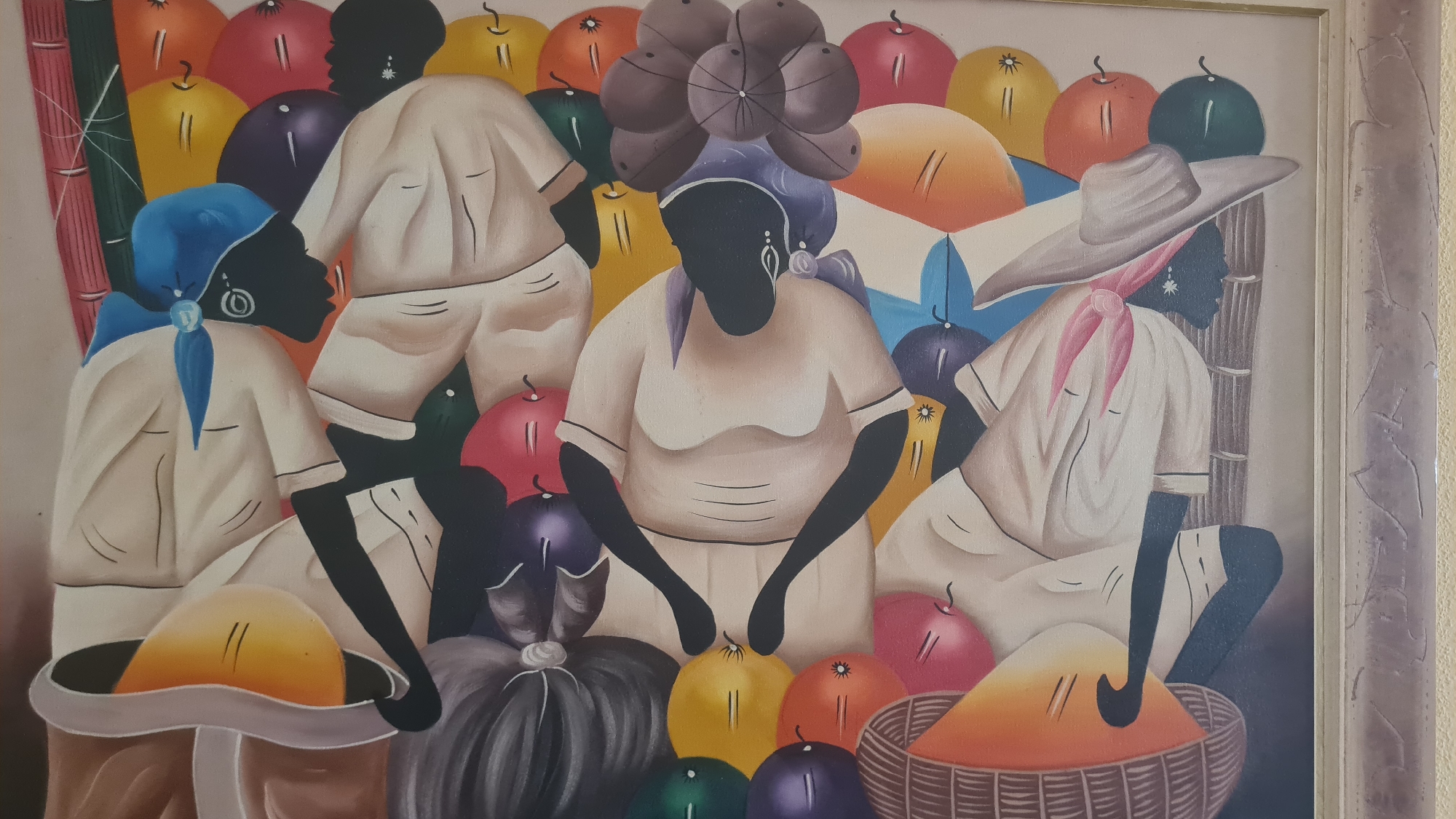 The image is a painting depicting a group of silhouetted figures, likely women, engaged in what appears to be a market scene. The figures are rendered in black and are dressed in loose-fitting, light-colored clothing. They are adorned with colorful headscarves and accessories, including earrings and necklaces. Surrounding the figures are a variety of brightly colored, round objects, suggestive of fruits or vegetables, as well as woven baskets. The style of the painting is somewhat stylized and folk-art-like, with bold outlines and vibrant colors. The background is simple and abstract, allowing the figures and their wares to be the focal point. There is no discernible urban environment or specific location evident in the painting itself, meaning it cannot be located in Elda, Spain, or any other city.