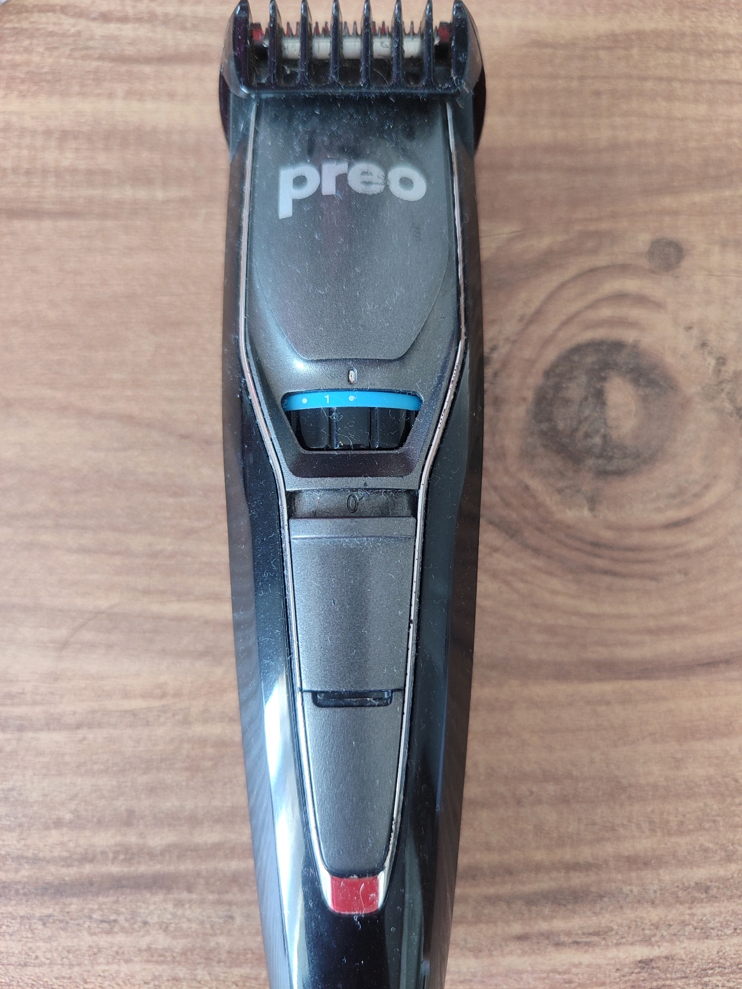 A black beard trimmer with the brand name "preo" is shown on a wooden surface. The trimmer has a comb attachment at the top, a dial with settings indicated by numbers 0 and 1, and a red accent at the bottom. The wooden surface has a visible wood grain pattern. This image was taken in Gümüşova, Turkey.