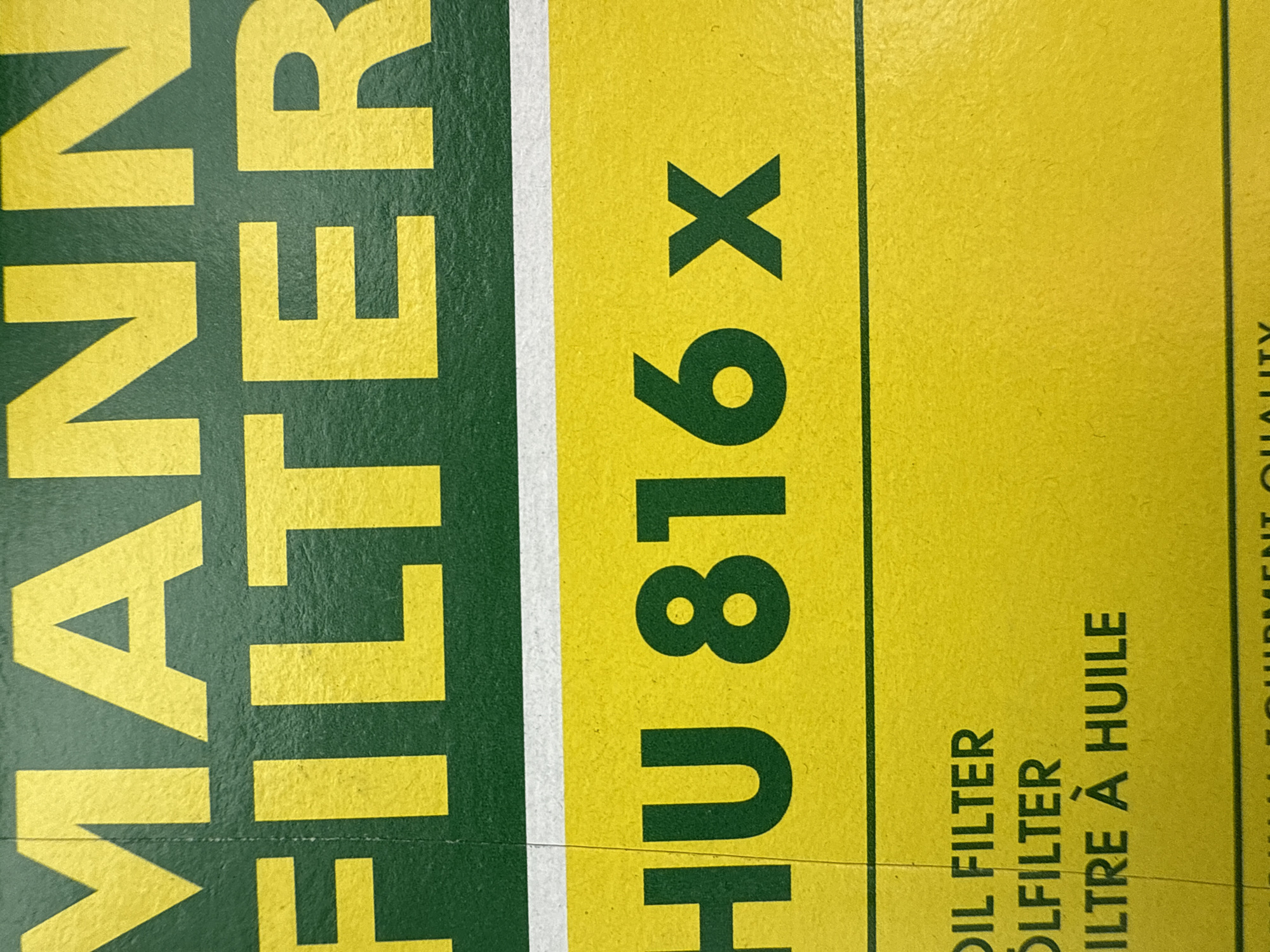 The image shows a portion of a MANN-FILTER product box, specifically displaying the text "MANN FILTER" in yellow letters on a green background, and "HU 816 x" in green letters on a yellow background. Beneath "HU 816 x", the phrase "OIL FILTER ÖLFILTER ILTRE À HUILE" is visible in black.
There is no information in the image that indicates the location in the city of Votkinsk, Russia.