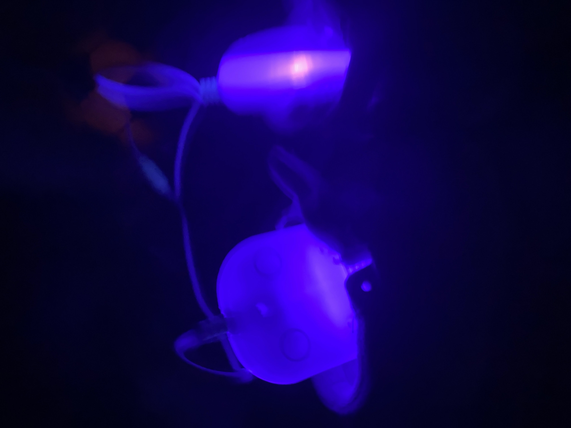 In a dimly lit environment, two Funko Pop figures are illuminated with a vibrant blue light. One figure is positioned above the other, connected by a thin white cord. The location and city are unknown.