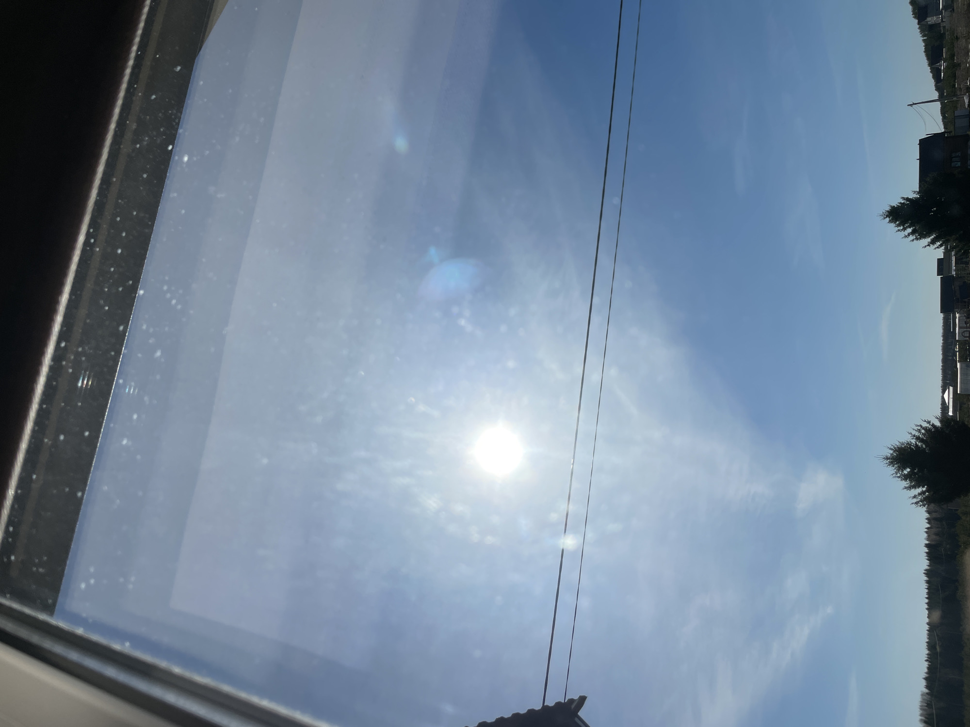 The image appears to be taken from inside a building or structure, looking out through a window. The window frame is visible on the left side of the image. The outside view shows a bright, sunny sky with scattered clouds. There are power lines visible in the sky. On the right side of the image, there is a line of trees. The information about the location in Подшивалово, Russia, is not discernible from the image.