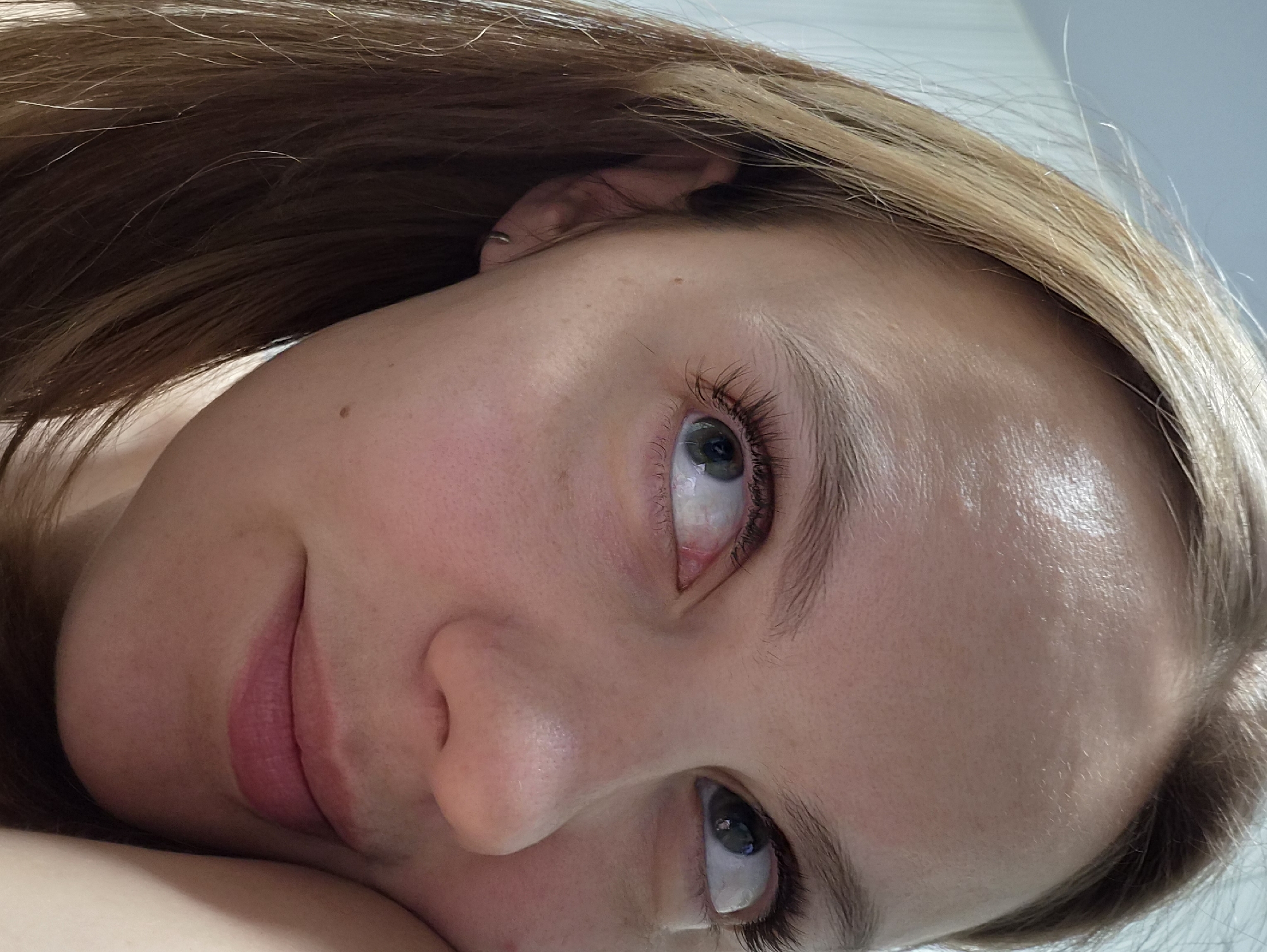 A close-up portrait of a fair-skinned woman with light brown hair, appearing to be lying down. Her face is tilted upward, with her eyes looking towards the upper left. She has light-colored eyes and natural makeup. An earring is visible in her left ear. The background appears to be a plain, light color. No specific identifiable elements indicate a location in Chaikovsky, Russia.