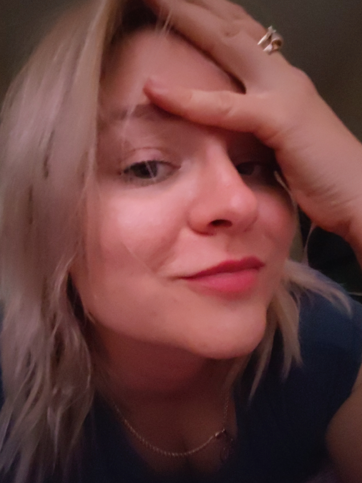 A close-up selfie of a blonde woman, partially obscured by her own hand on her forehead. She wears a ring on her finger. A necklace is visible around her neck. The environment is indistinct. The image does not provide information about the city of Izhevsk, Russia.