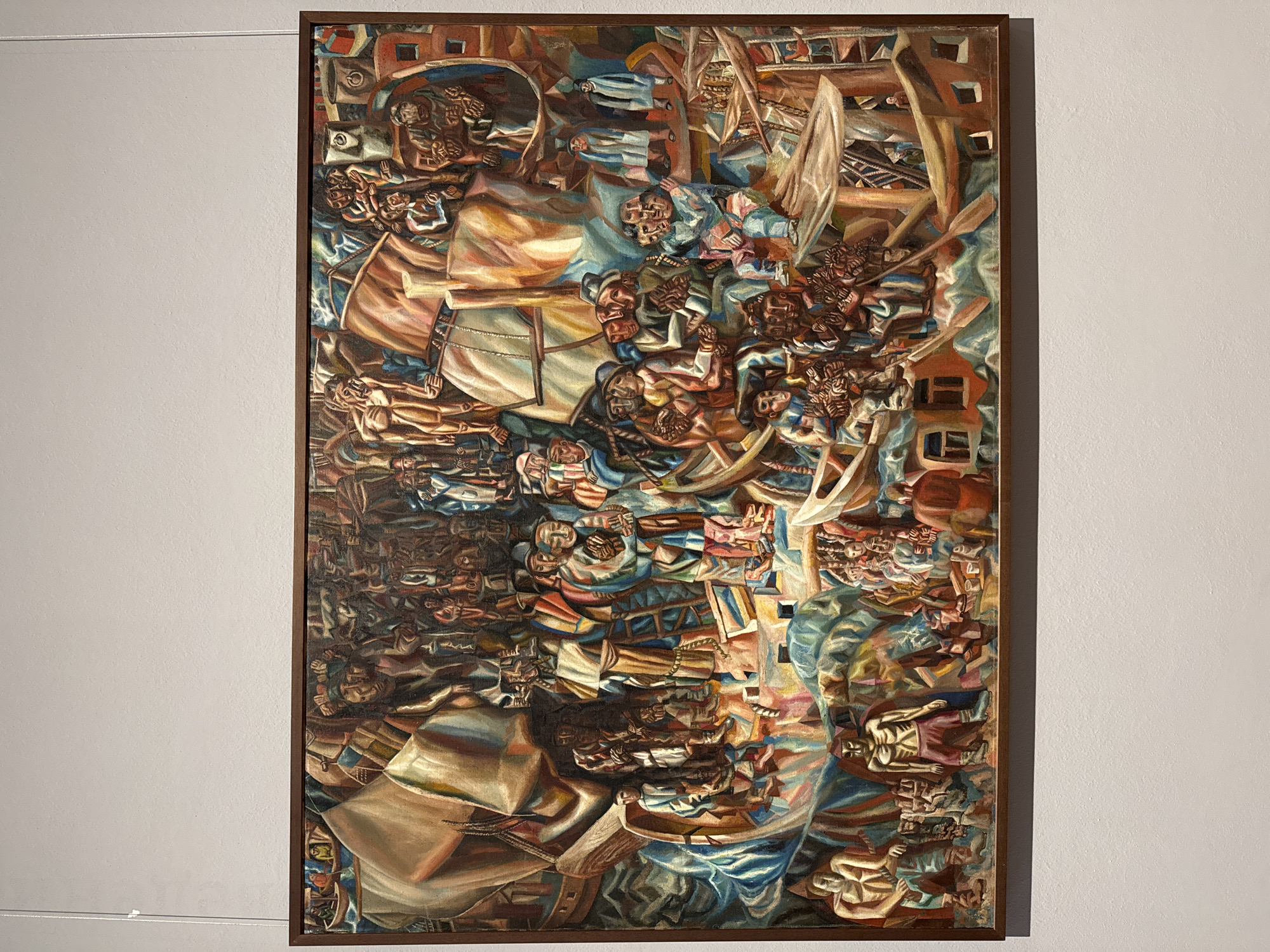 This is a vertical, rectangular oil painting framed in dark wood, displayed on a white wall. The artwork depicts a chaotic and crowded scene rendered in an expressionistic style with Cubist influences. Numerous figures are densely packed, overlapping and intertwined, creating a sense of overwhelming activity. The figures are stylized and abstract, with some appearing to be in distress or in various states of movement and repose.
The color palette is rich and varied, featuring earthy browns, warm oranges, deep blues, and touches of red and yellow, with areas of light and shadow adding depth and drama. The brushstrokes are visible, contributing to the textured and energetic feel of the painting. The composition is complex, with a sense of upward and downward movement, and fragments of architectural elements or ship-like structures are integrated into the scene. Some figures are depicted with skeletal or emaciated forms, suggesting themes of suffering or mortality. The overall impression is one of a dramatic, possibly tumultuous, event involving a large group of people in an ambiguous setting. There is no visible text in the painting, nor clear indications of time of day, weather, or specific location beyond the context of Moscow, Russia. The emotions conveyed are largely intense and somber, hinting at struggle or a shared, dramatic experience.