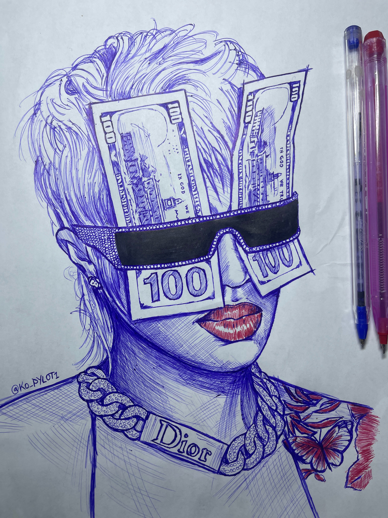 The image is a drawing in blue and red ink on a white surface. It depicts a stylized portrait of a person from the shoulders up. The person has a voluminous, wavy hairstyle suggested by blue ink lines. Their eyes are covered by two US $100 bills, drawn to resemble sunglasses. The bills are positioned vertically, with the denomination "100" clearly visible on each. The person's nose is partially obscured by the bills, and their lips are painted a vibrant red. They are wearing a chunky chain necklace with a "Dior" pendant. A tattoo of a butterfly and leaves, rendered in red and blue ink, is visible on their right shoulder and neck area. The drawing includes a watermark or signature in the lower left corner that reads "@KO_PYLOT1". To the right of the portrait, three pens are visible: one blue, one clear, and one pink, with their caps on. The drawing is done on a flat surface, possibly paper, which has some subtle wrinkles and texture. There is no indication of the city of Jos, Nigeria, in the image itself.