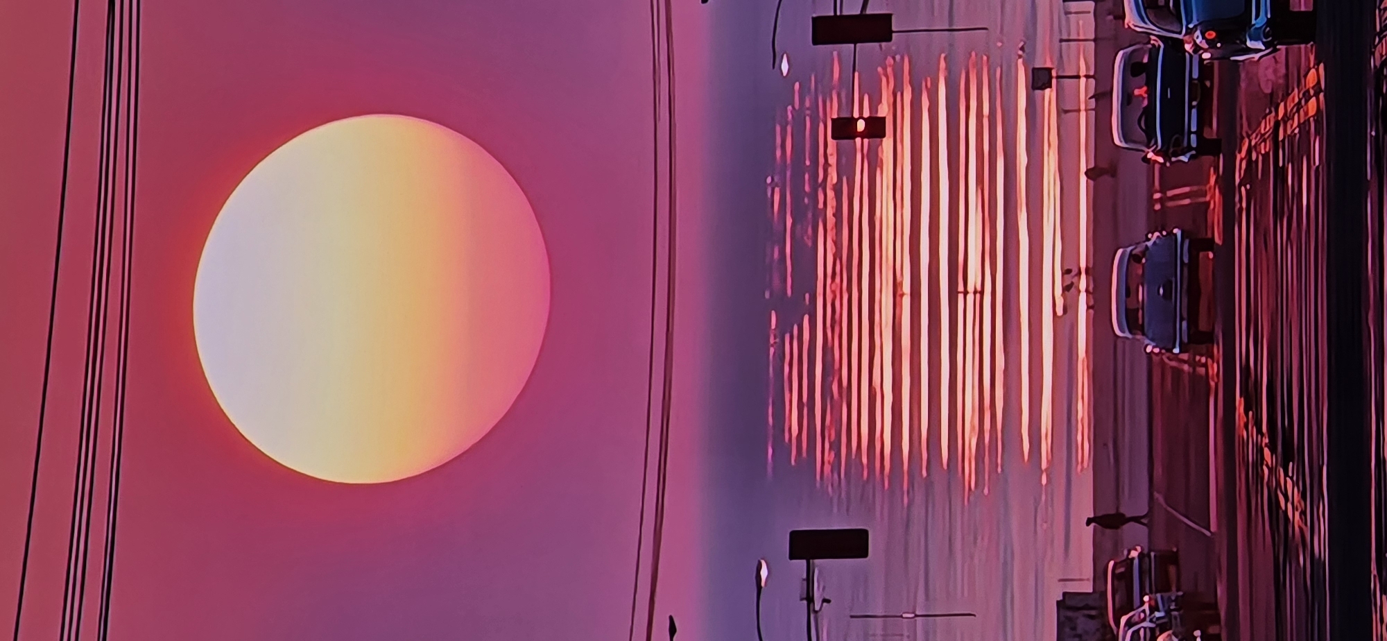 The image captures a surreal sunset scene with a large, glowing orb, likely the sun, dominating the left side. The orb transitions in color from a pale yellow at its center to pink and purple at its edges. Several thin, black lines run vertically to the left of the orb, possibly representing power lines or wires.
The right side of the image depicts a body of water, likely a lake, reflecting the vibrant colors of the sunset. Vertical streaks of pink and red light, the reflections of an unseen structure or lights, create a striking visual effect on the water's surface. In the foreground on the right, a street scene is visible, with several cars parked or driving in what appears to be a traffic jam or at a standstill. The reflections from the water continue onto the road surface. Traffic lights are also visible, some illuminated, adding to the urban feel of this section of the image. The overall mood is dreamlike and atmospheric, with the intense colors suggesting a dramatic end to the day. The time of day is clearly sunset, and the weather appears calm, with the water being still enough to produce clear reflections. No visible text is present in the image.