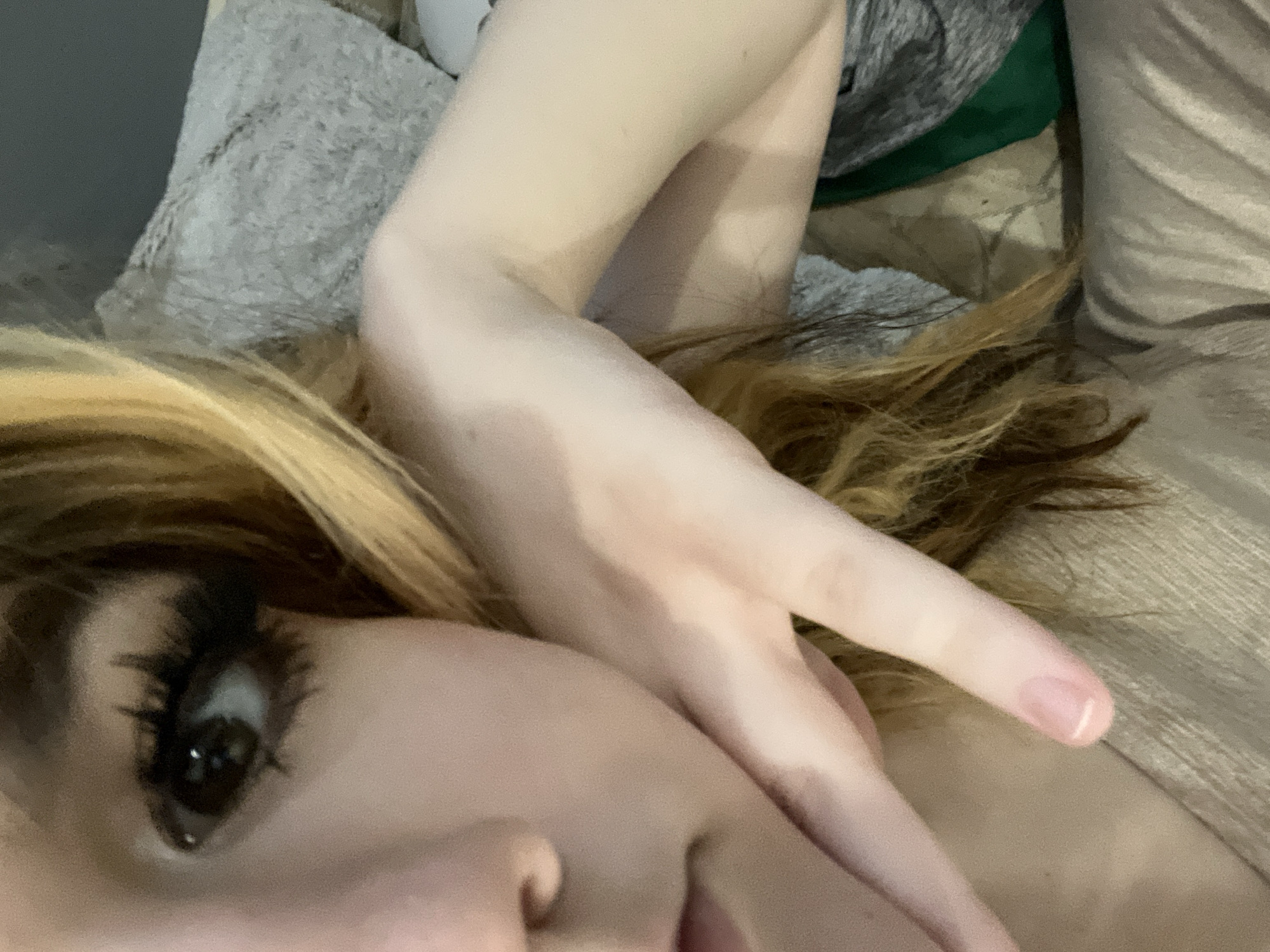 The image shows a close-up perspective of a person lying down. The visible portion of the person includes their face, with focus on a dark brown eye with prominent eyelashes, a nose, and lips. Part of their blonde and brown-toned hair is visible near their face. The person's arm and hand are positioned close to their face. The setting appears to be indoors, with a textured pillow behind the person and a blanket covering them. No specific details indicate the location is Calgary, Canada.