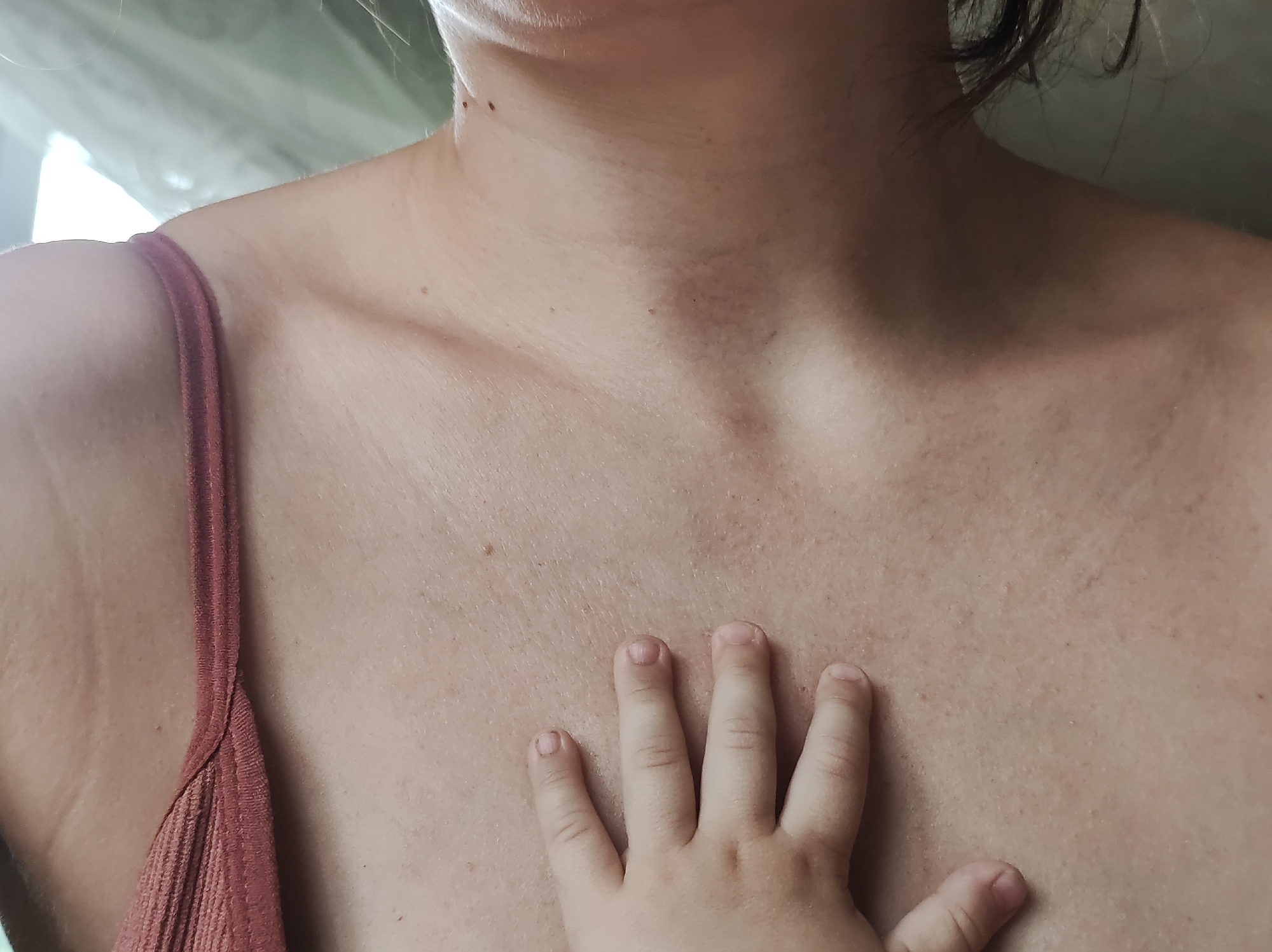 A close-up shot depicts the upper torso and chest of a light-skinned individual wearing a camisole. A child's hand rests on the center of the chest. There is no indication that this image was taken in Фоки, Russia.