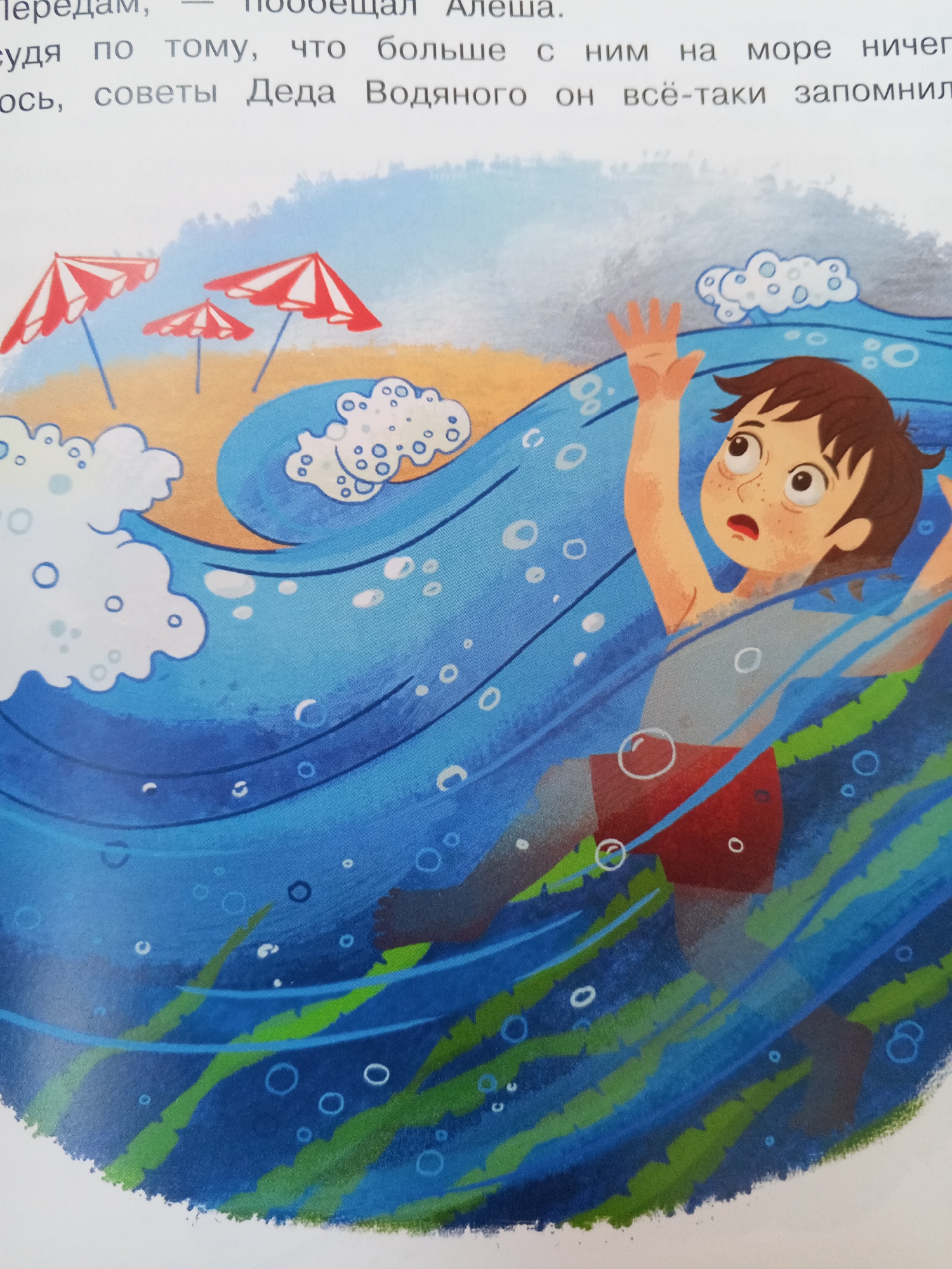 The image depicts a young boy, identified as Alesha, struggling in a large wave in the sea. He is shown with his arms raised in distress, his mouth open, and his eyes looking upwards. He is wearing red swim trunks. The water is depicted as turbulent with white foam and bubbles. In the background, a sandy beach is visible with three red and white striped beach umbrellas. The text in the image is in Russian and appears to be part of a story, mentioning Alesha and advice from "Grandpa Vodyanoy" related to the sea. The scene is an illustration and does not depict a specific location in Chistopol, Russia; it is a general depiction of a beach and sea scenario.