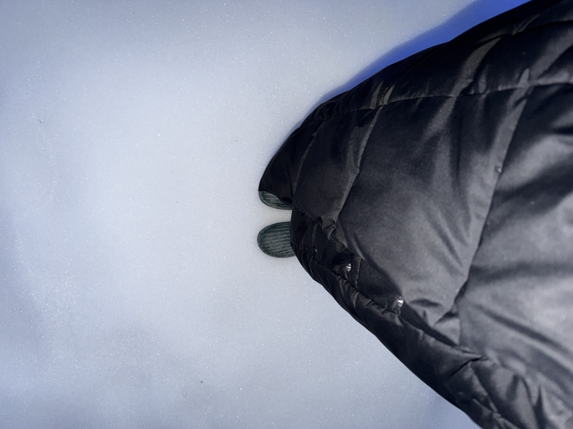 A view from above shows a person standing in the snow. The person is wearing a black puffy jacket, and their feet are visible. The location appears to be outdoors, in a snowy environment. It is not possible to confirm the location as the city of Chaikovsky, Russia from the image alone.