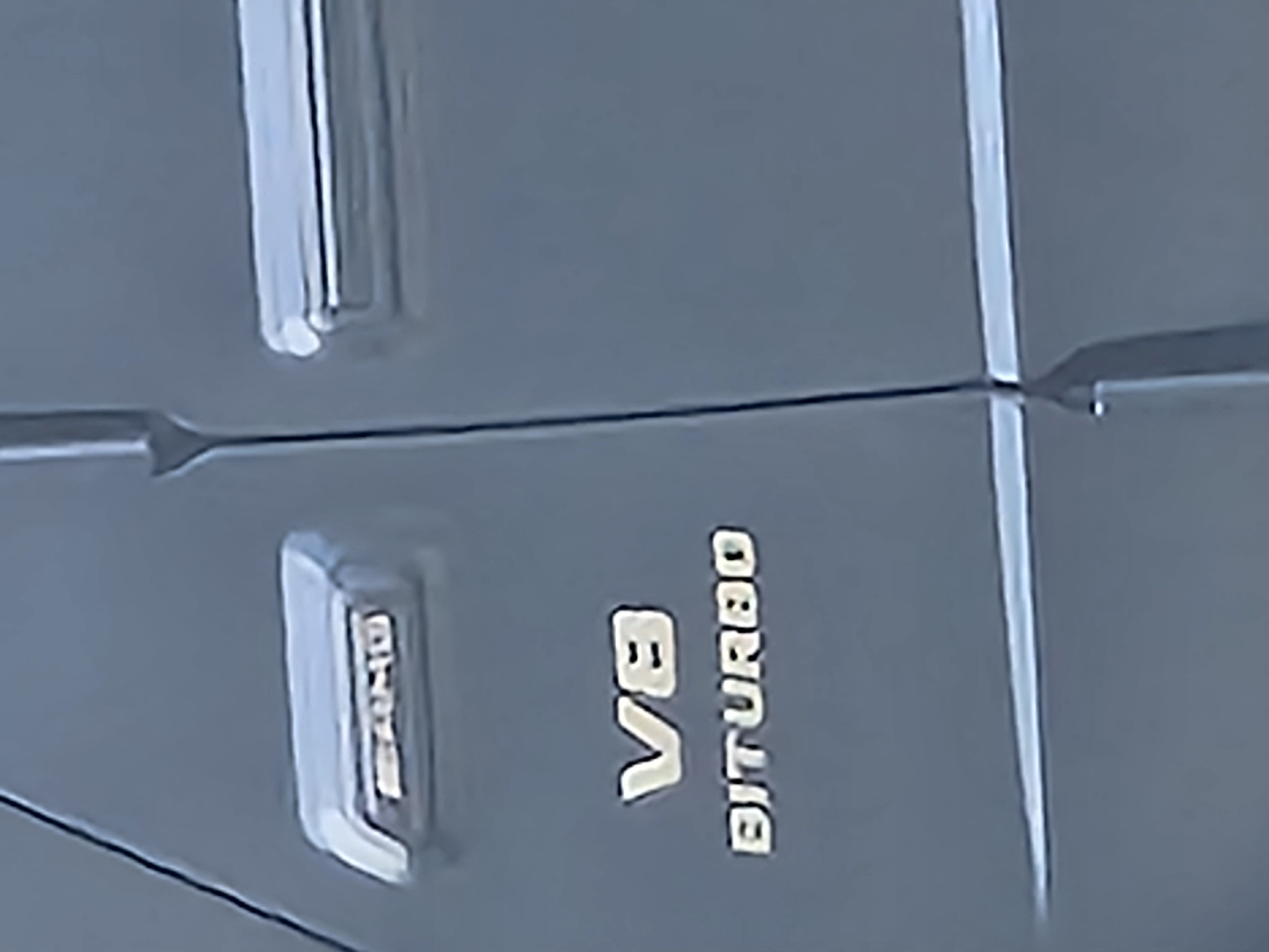 The image shows a close-up of the side of a gray Mercedes-AMG car. The words "AMG" and "V8 BITURBO" are visible on the side. The location is unknown, so I cannot confirm if it is located in Witton Gilbert, United Kingdom.