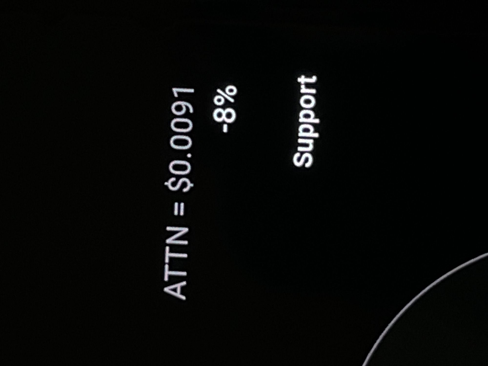 The image shows a black screen with white text. The text reads "ATTN = $0.0091 -8% Support". The text is positioned in the upper and middle right portions of the screen. A curved white line is visible in the lower left corner of the screen. There is no discernible location in the city of Dhaka, Bangladesh.
